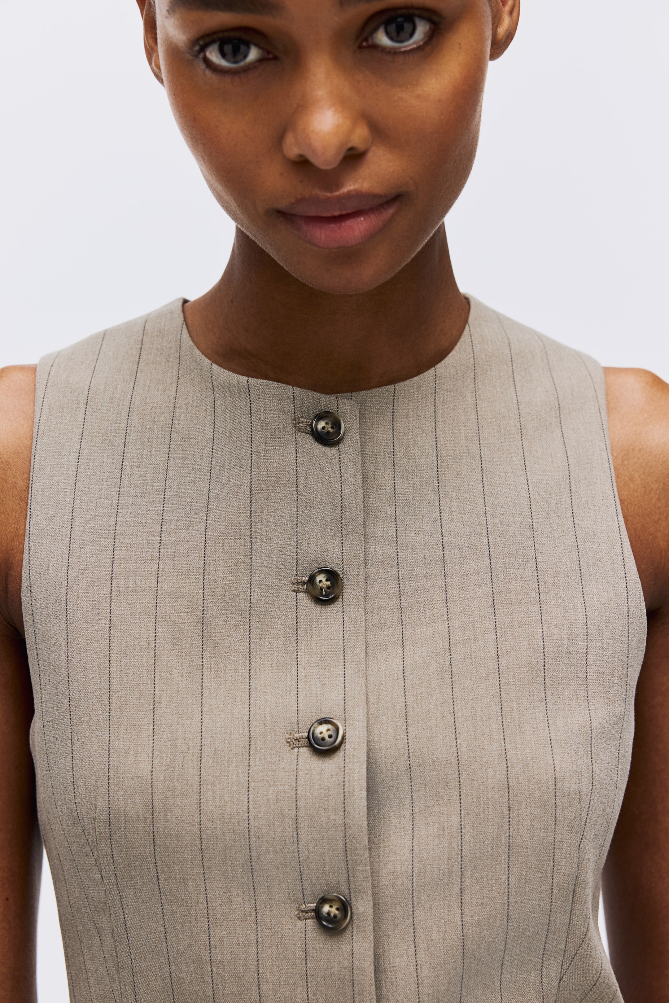 Преглед на по-голямо изображение: Безръкав бежов топ с фини райета, кръгло деколте и предна планка с четири видими тъмни мраморирани копчета.