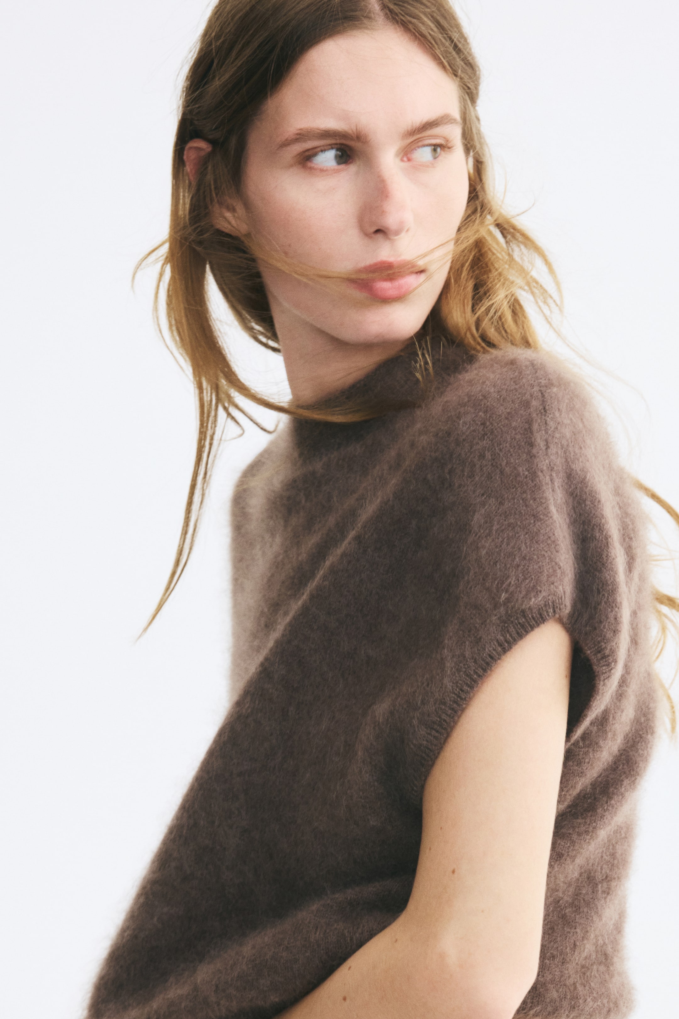 View larger image: A brown, fuzzy knitted wool vest featuring a high neck and ribbed detail around the armholes is worn by the model. The oversized vest showcases a soft, textured finish as the model turns slightly to the side.