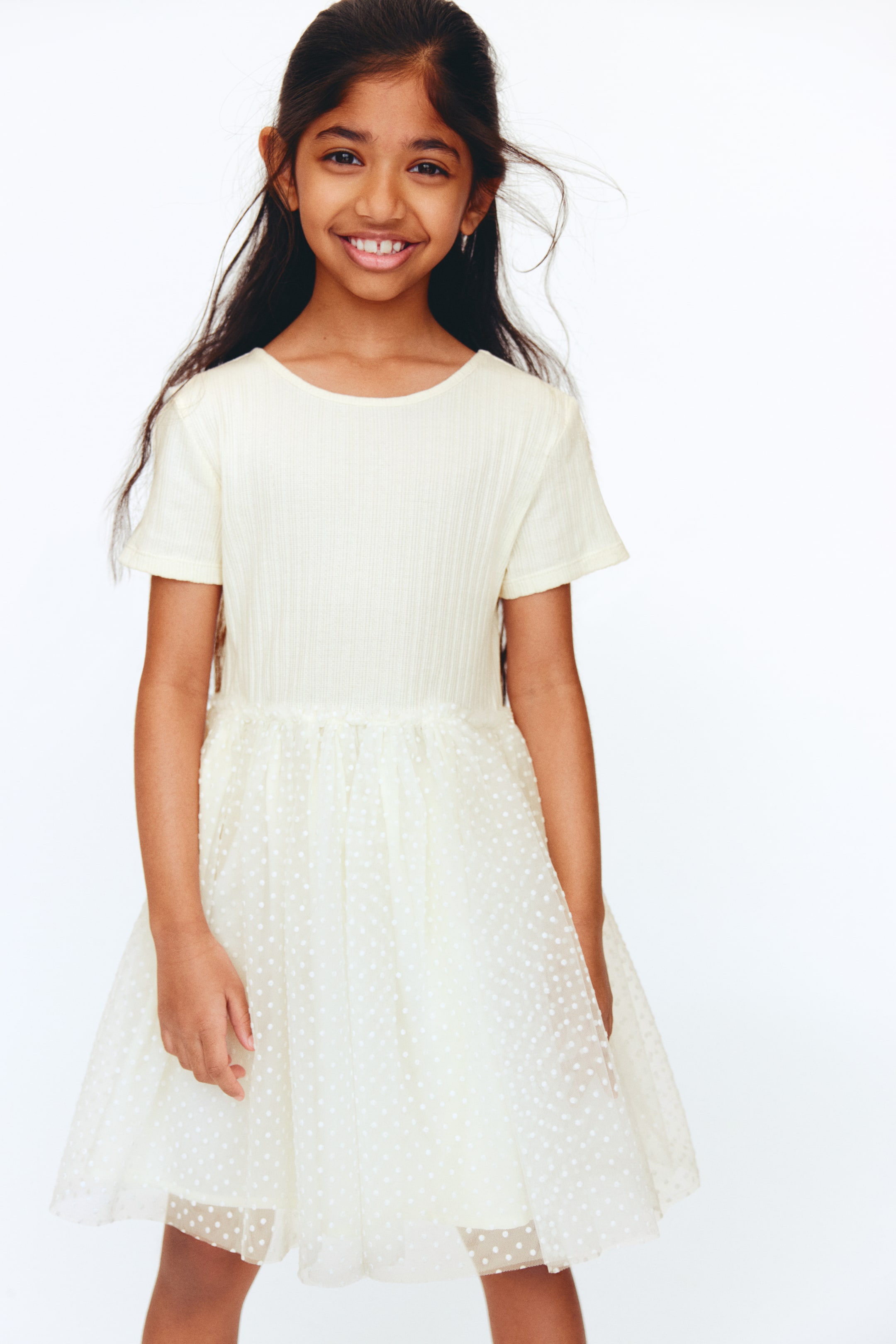 Visa större bild: Den krämfärgade klänningen har en ribbad kortärmad topp och en rynkad midja. Kjolen har ett genomskinligt överdrag med vita prickar över ett ogenomskinligt foder.