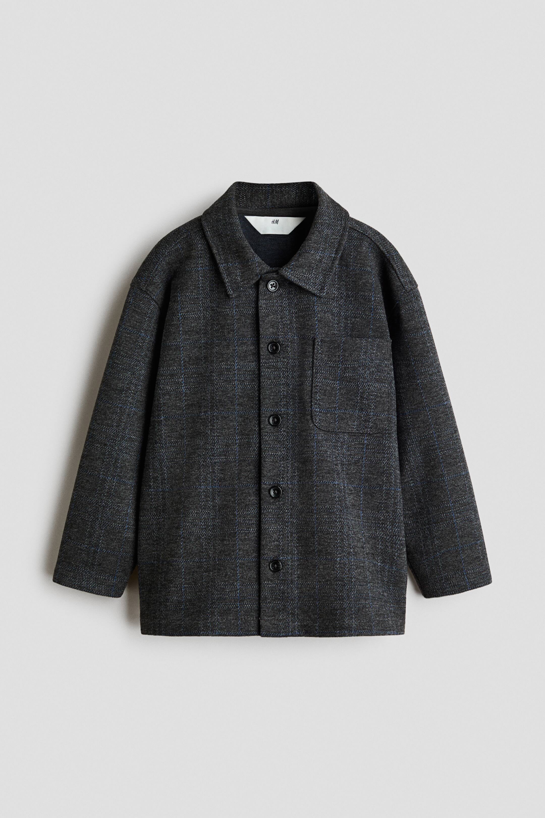 View larger image: A loose-fit overshirt in dark grey textured jersey is shown from the front, featuring a subtle blue grid pattern. It has a classic collar, button-down front, a single chest patch pocket, and dropped shoulders with long sleeves.