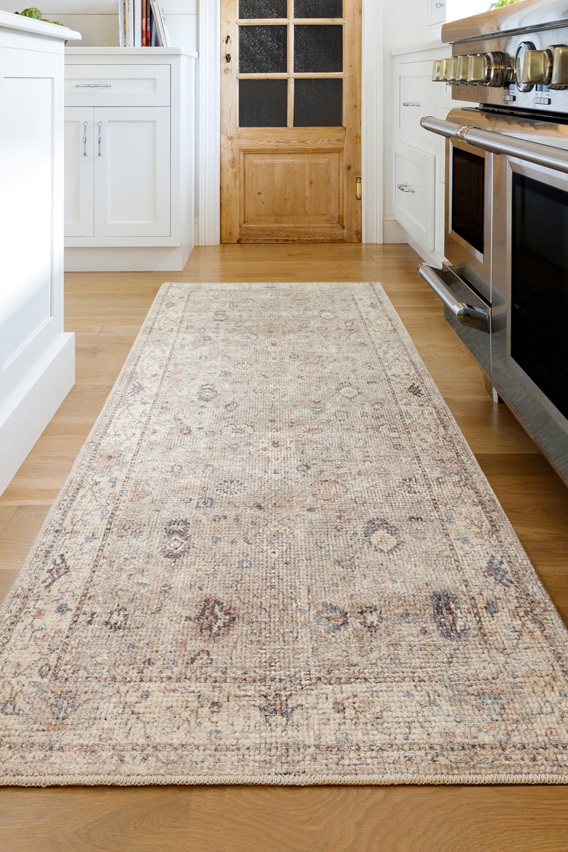 View larger image: A runner rug is displaying a distressed traditional pattern in muted beige, blue, and brown tones. It is lying flat, extending from the foreground into the background.