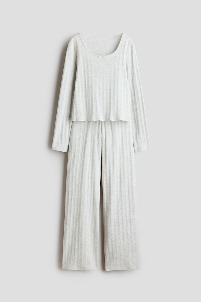 A light grey pointelle knit pyjama set is shown in a front view, featuring a matching long-sleeve top and straight-leg trousers. The top is designed with a scoop neckline accented by a small white satin bow at the centre, highlighting the soft, vertically textured fabric of the coordinated set. - 1