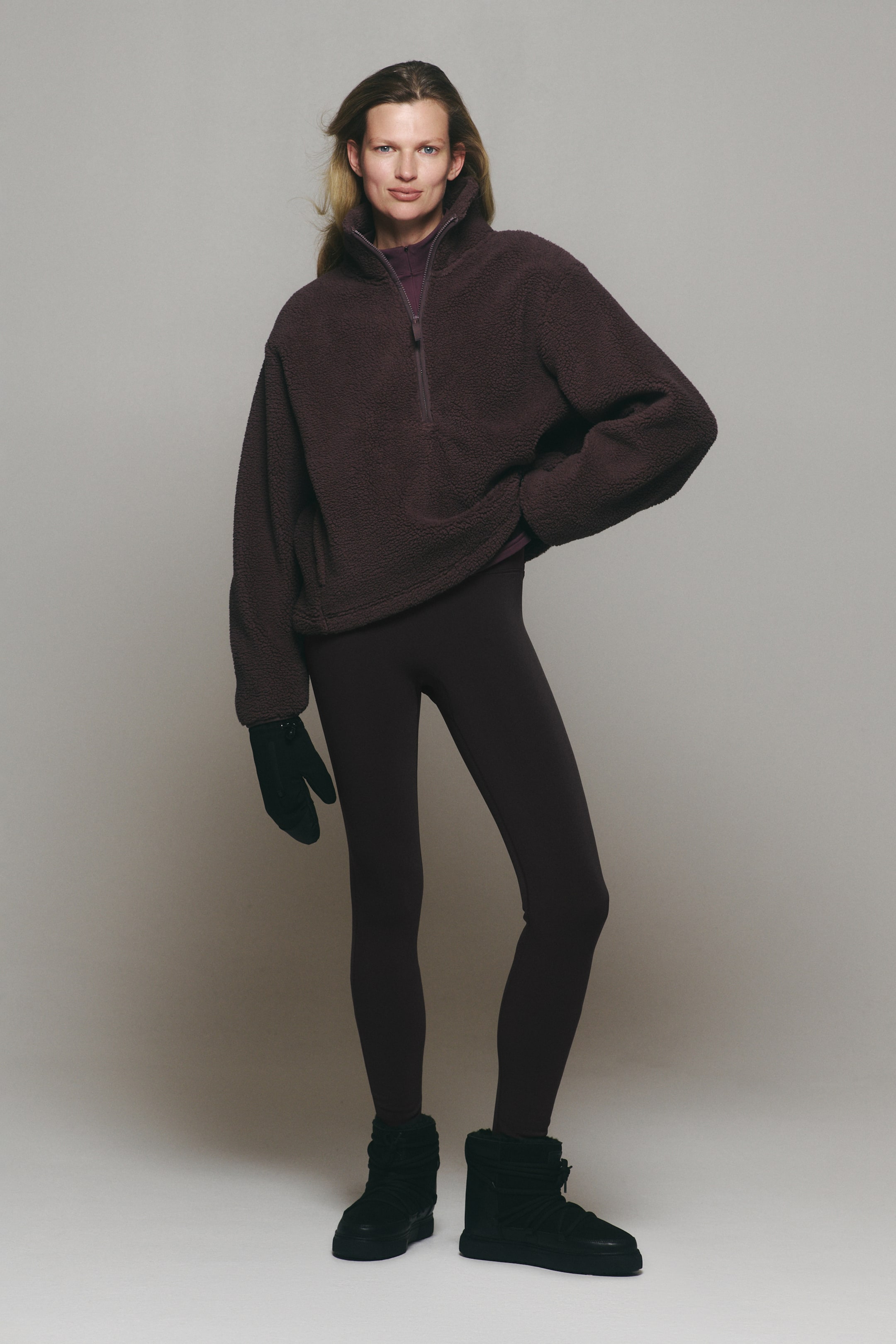 View larger image: The model is wearing a dark plum fleece half-zip pullover paired with matching leggings. This cold-weather outfit is styled with black winter boots and black gloves.