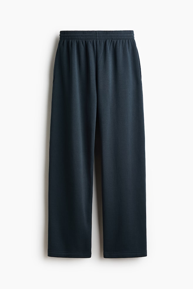 Dark blue pants are hanging vertically, facing front. They are featuring an elasticized waistband with gathering and visible side slash pockets. The pants have a straight, wide-leg cut with a plain hem. - 1