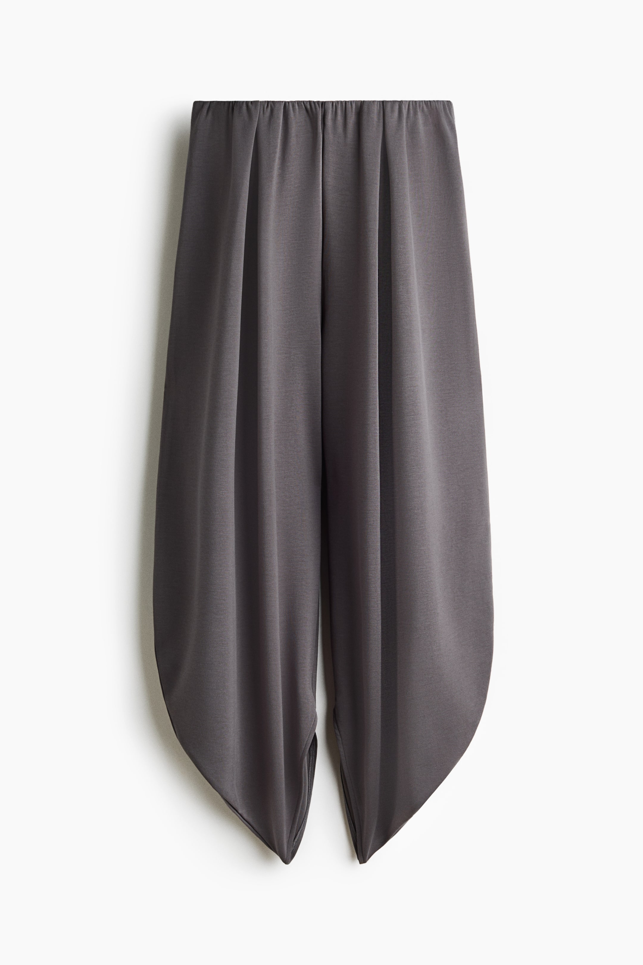 Xem ảnh lớn hơn: Một chiếc quần dài xám đậm dáng drape đang được chụp chính diện, nổi bật với cạp chun nhún và các ly sâu tạo nên phom dáng bồng bềnh, uyển chuyển. Ống quần thu nhỏ dần về phía gấu cong nhọn, làm nổi bật cấu trúc mềm rũ của chất liệu vải.