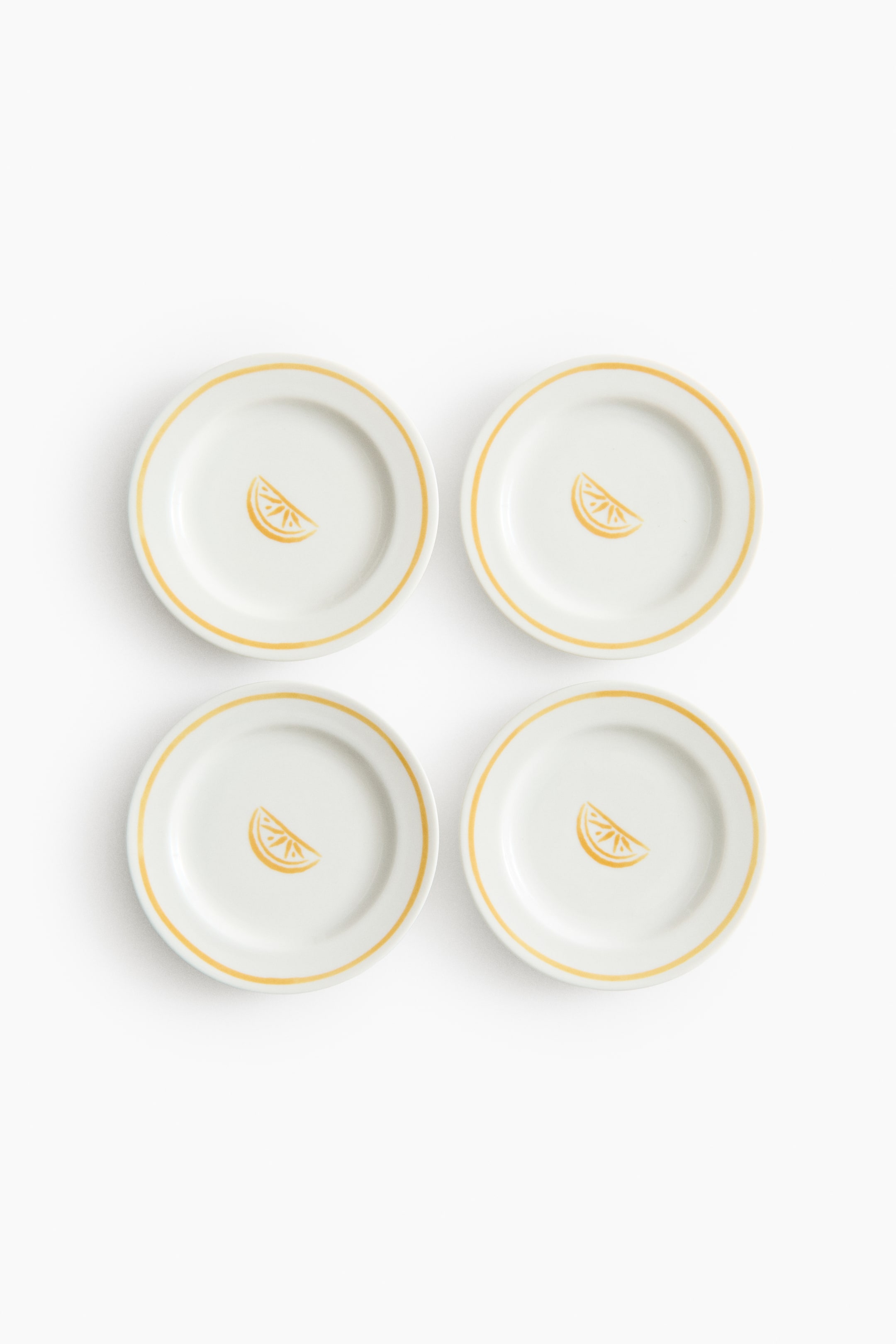 View larger image: A set of four small porcelain plates is displayed as FRONT, each showcasing a white base with a yellow painted rim and a yellow lemon slice print in the center.