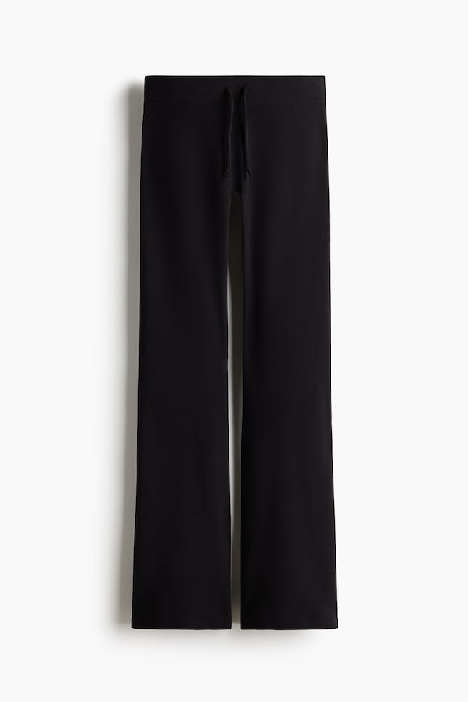 A pair of black wide-leg trousers is hanging in a front view, featuring a flat waistband with matching drawstrings and displaying a relaxed, slightly flared silhouette. - 1