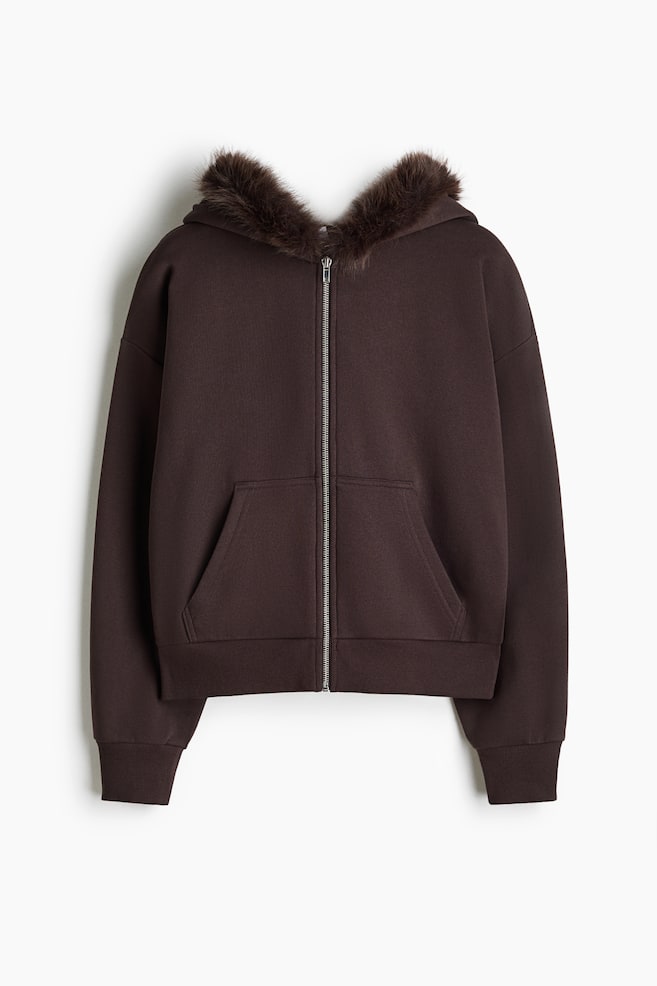 Ein dunkelbrauner Hoodie mit ReiÃverschluss ist von vorne zu sehen und verfÃ¼gt Ã¼ber eine weiche Kunstfell-Besatzung entlang der Kapuze. Das Design zeigt einen silberfarbenen MetallreiÃverschluss, eine geteilte KÃ¤ngurutasche, Ã¼berschnittene Schultern sowie gerippte BÃ¼ndchen und Saum. - 1