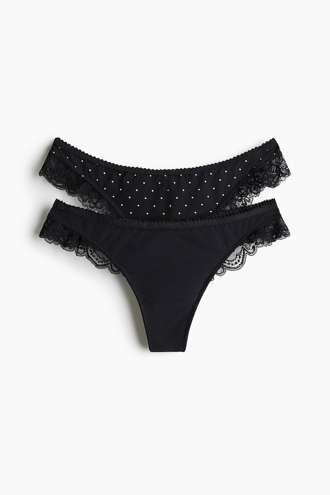Un lot de deux culottes noires est présenté de face, avec une paire noire unie et une paire ornée dâun motif à pois blancs. Les deux modèles présentent une finition en dentelle noire festonnée au niveau des ouvertures des jambes ainsi quâune fine taille élastiquée. - 1