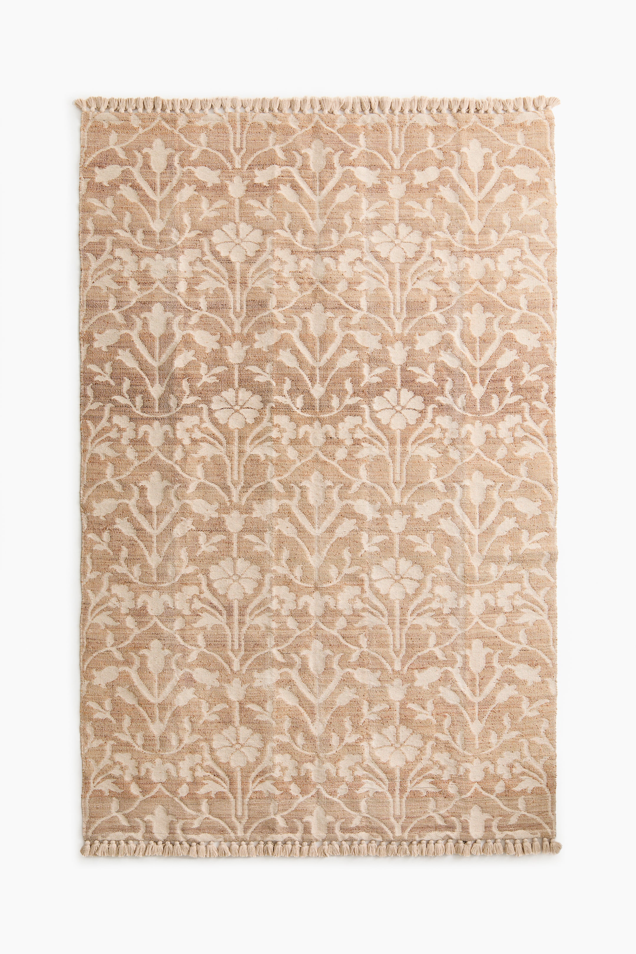 View larger image: A large rug features a repeating floral pattern in a light tone, contrasting with its natural jute and cotton-blend weave. It is fringed on both short ends.