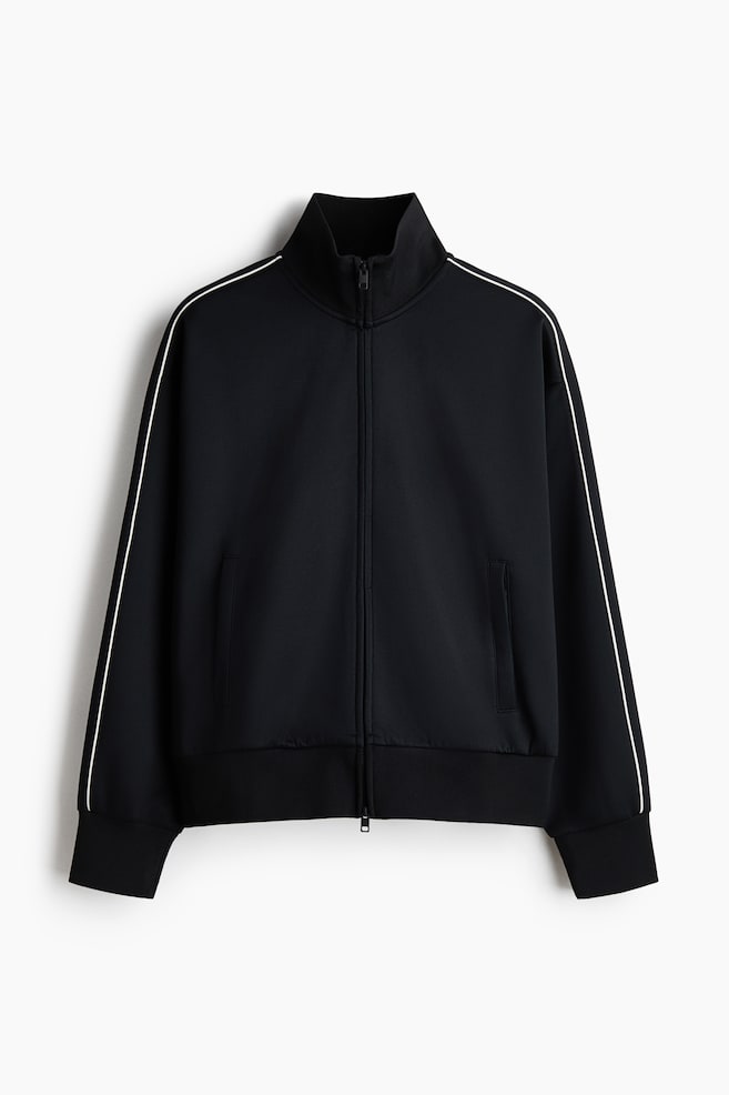 Eine schwarze Trainingsjacke wird von vorne gezeigt und verfügt über einen durchgehenden Reißverschluss und einen Stehkragen. Ein einzelner weißer Streifen verläuft entlang jedes langen Ärmels, und zwei vordere Paspeltaschen sind sichtbar. Gerippte Bündchen und ein gerippter Saum vervollständigen das Design. - 1