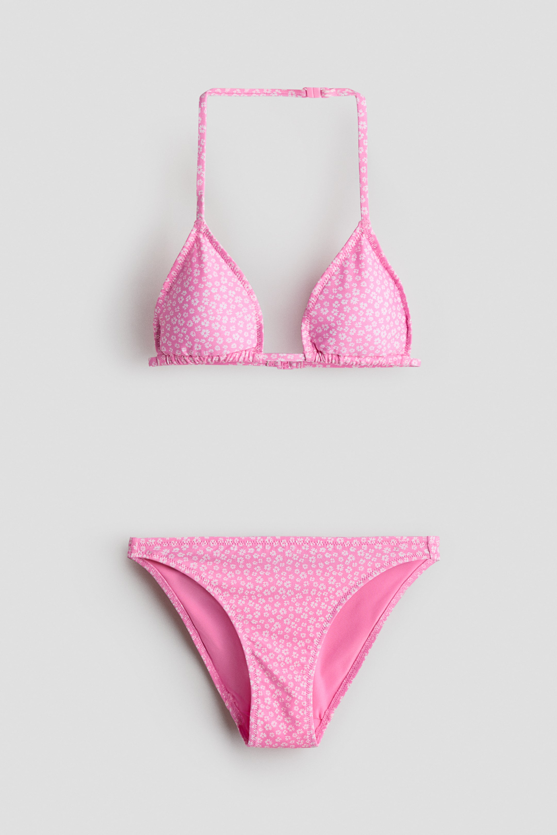 Grotere afbeelding bekijken: Een bikiniset toont zijn vooraanzicht. De roze driehoekige bikinitop, met een wit bloemenpatroon, heeft een verstelbare halternekband met een roze plastic sluiting, en bijpassende roze bikinibroekjes maken de set compleet.