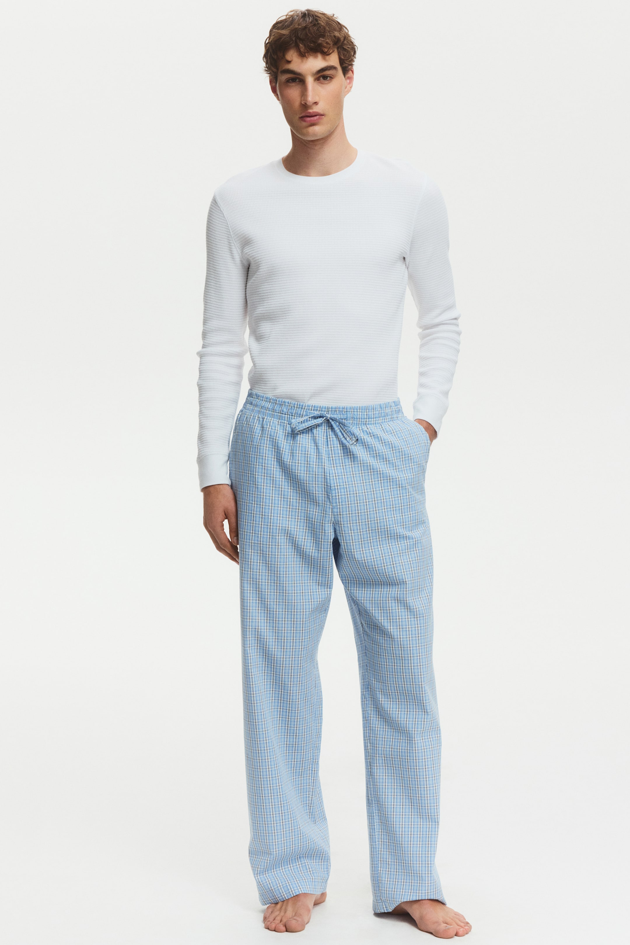 View larger image: Light blue plaid pajama pants feature an elasticized waistband with a visible light blue drawstring. The pants showcase a relaxed, straight-leg fit and side pockets.