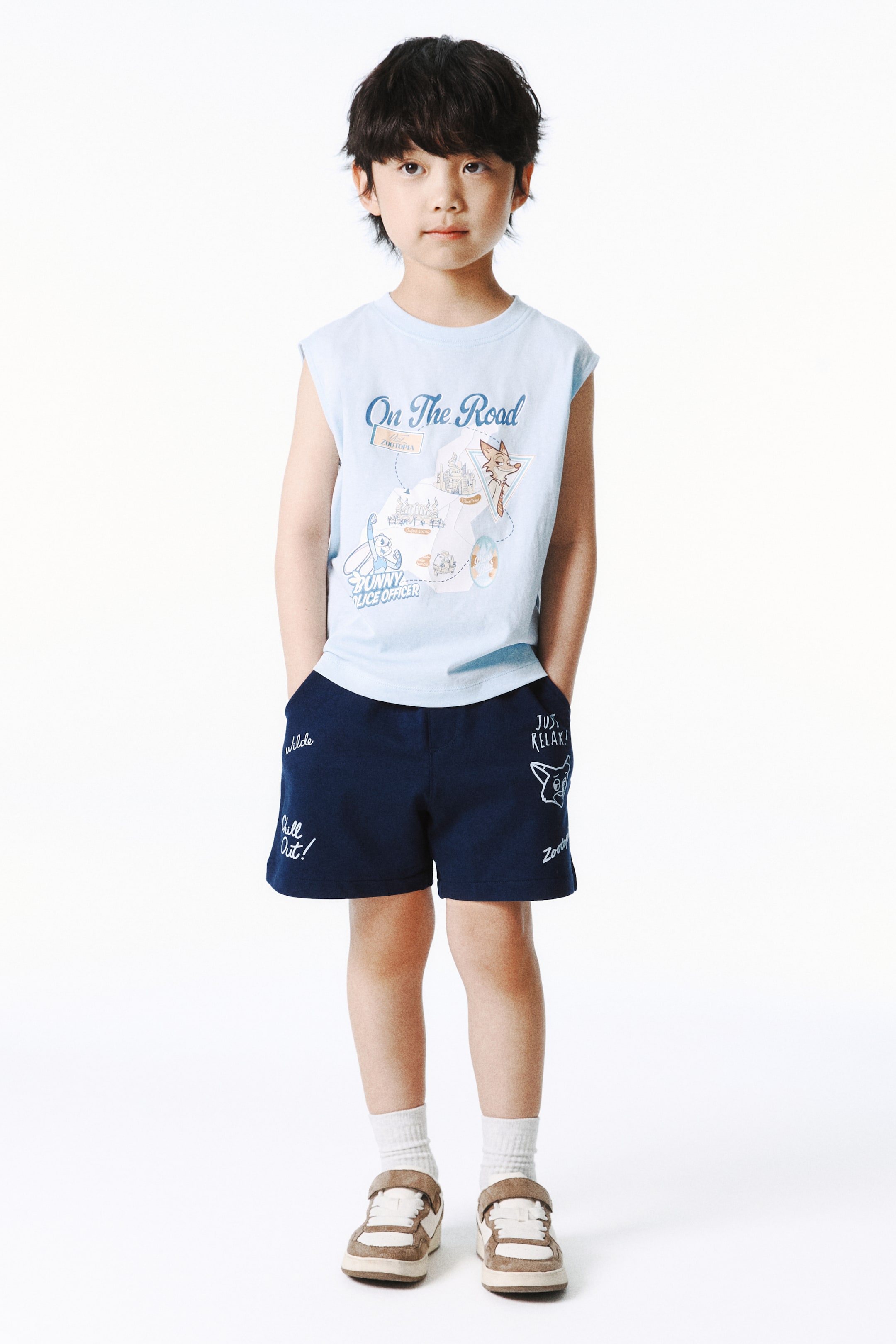 View larger image: A light blue sleeveless t-shirt menampilkan grafik "On The Road" dari Zootopia dengan watak Judy Hopps dan Nick Wilde. Ia ditunjukkan dari hadapan bersama seluar pendek kasual biru gelap, yang memaparkan teks putih dan lakaran watak pada kaki.
