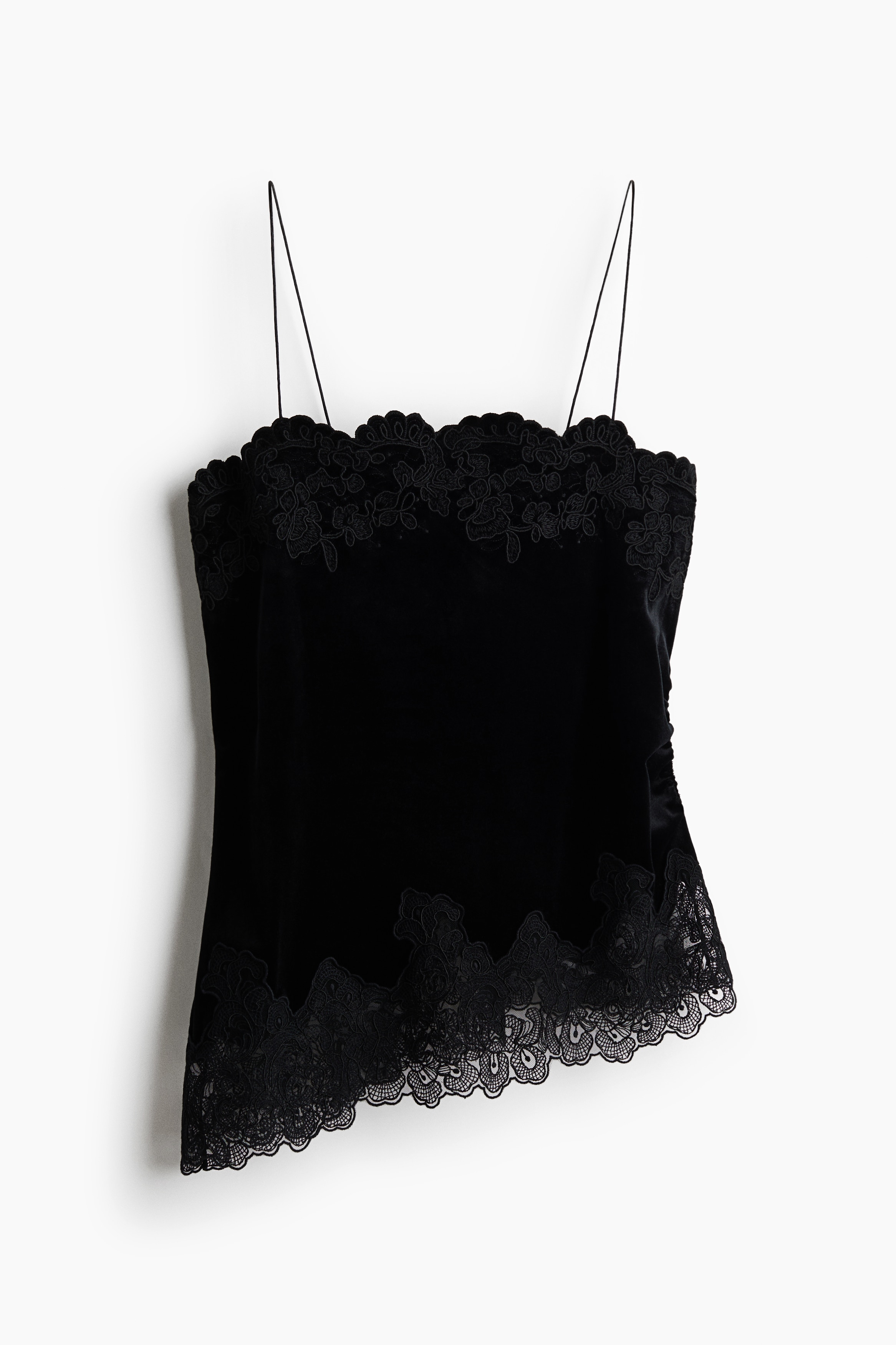 La modella indossa un top pigiama nero in velluto, caratterizzato da sottili spalline spaghetti, scollo dritto con profilo in pizzo e orlo asimmetrico rifinito in pizzo. Il top è abbinato a pantaloni larghi in velluto coordinati, anchâessi rifiniti in pizzo sullâorlo.