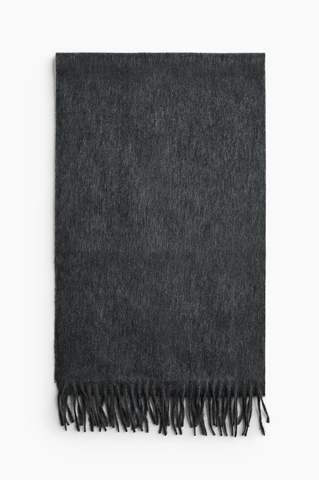 Une Ã©charpe en cachemire gris foncÃ© est prÃ©sentÃ©e de face, Ã  plat, afin de mettre en valeur sa texture douce et brossÃ©e. LâÃ©charpe prÃ©sente un dÃ©tail de franges torsadÃ©es le long du bord infÃ©rieur visible. - 1
