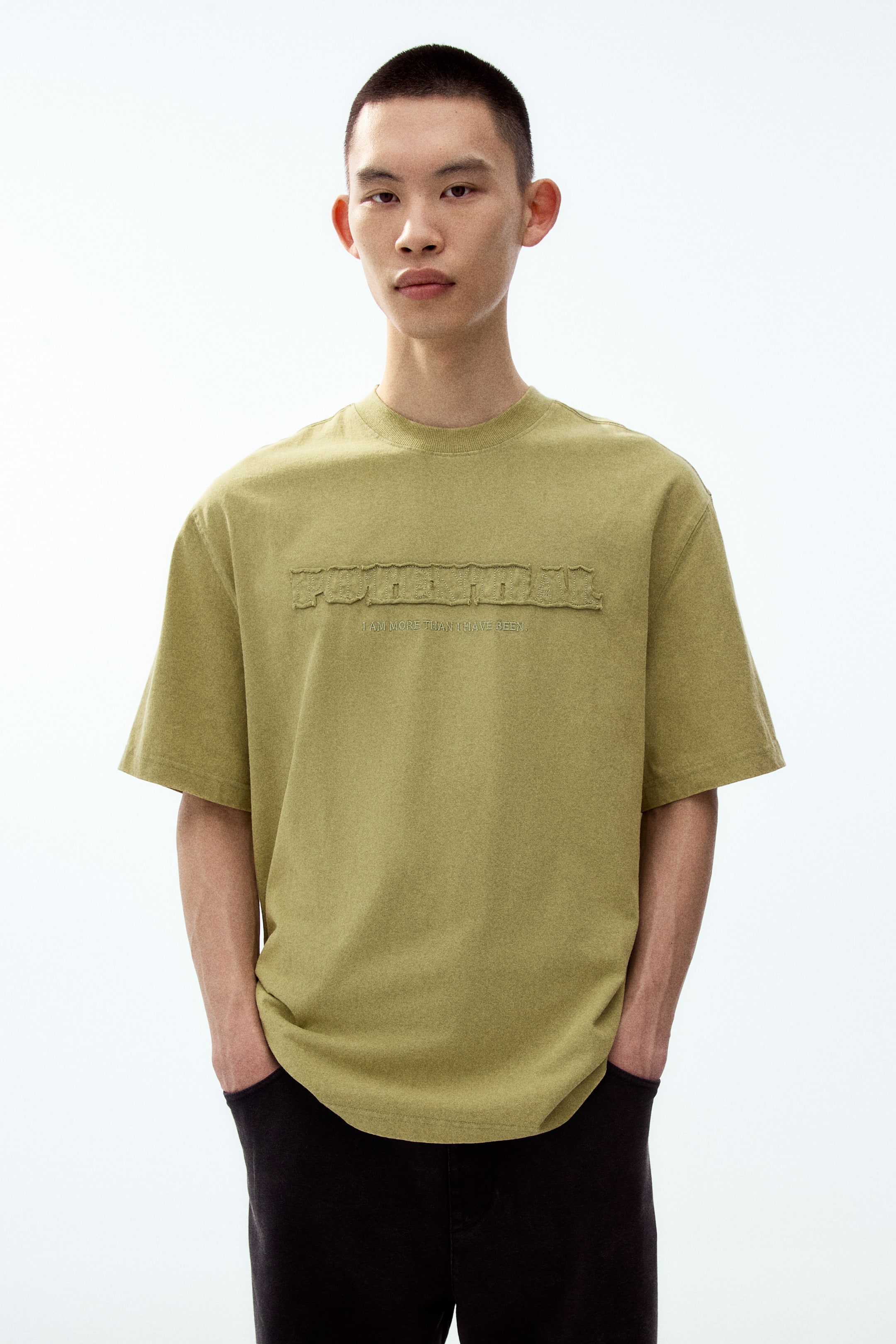 View larger image: A front-facing, olive-green textured short-sleeved t-shirt features a relaxed fit and a crew neck. An embossed "FOREVER" graphic with distressed edges is displayed across the chest, with the smaller text "I AM MORE THAN I HAVE BEEN" appearing just below it.