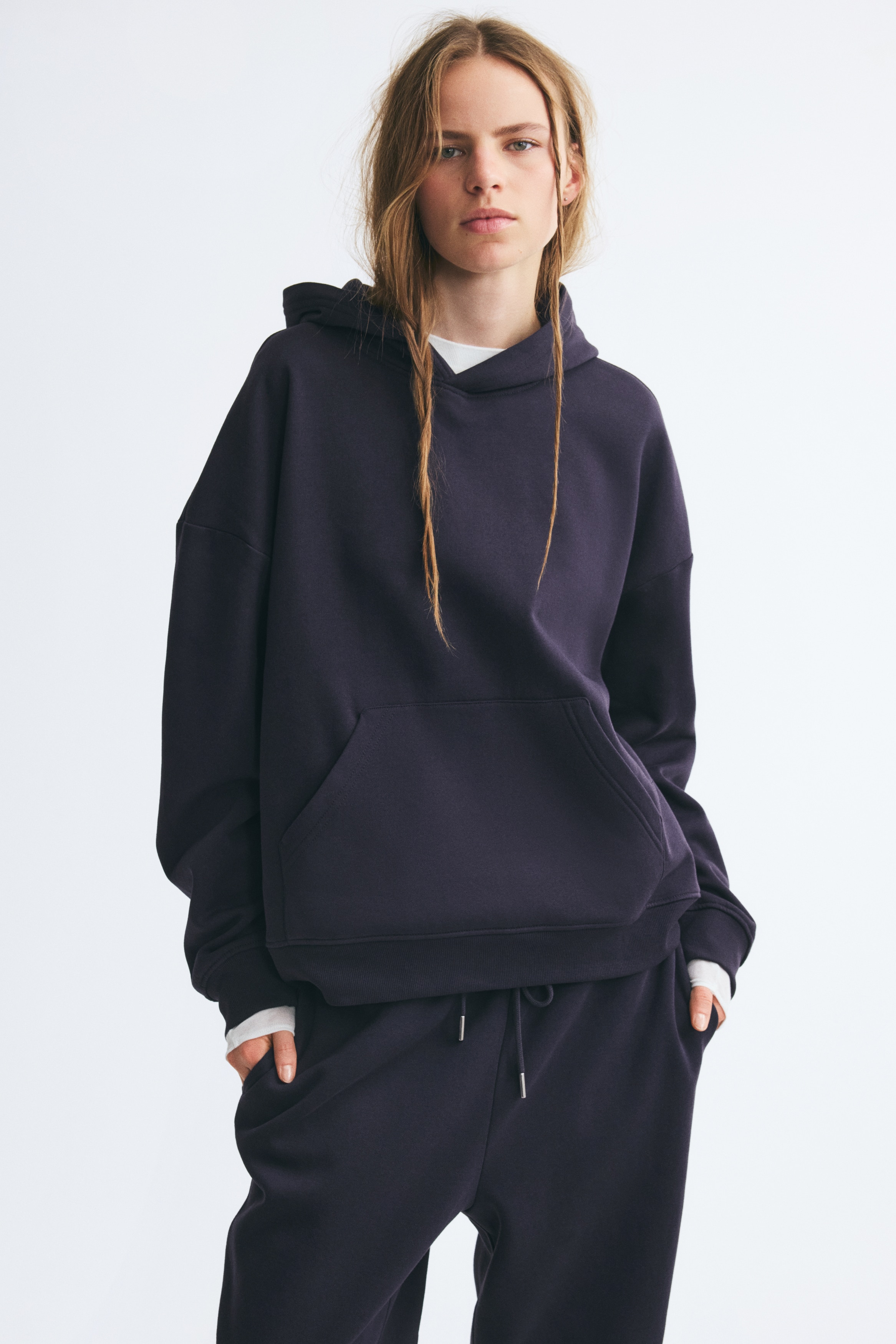 Ein dunkel marineblauer Hoodie wird von vorne gezeigt und verfÃ¼gt Ã¼ber eine doppellagige Kapuze, tief angesetzte Schultern und eine zentrale KÃ¤ngurutasche. Das Design wird durch RippbÃ¼ndchen an den Ãrmeln und einen gerippten Saum abgerundet.