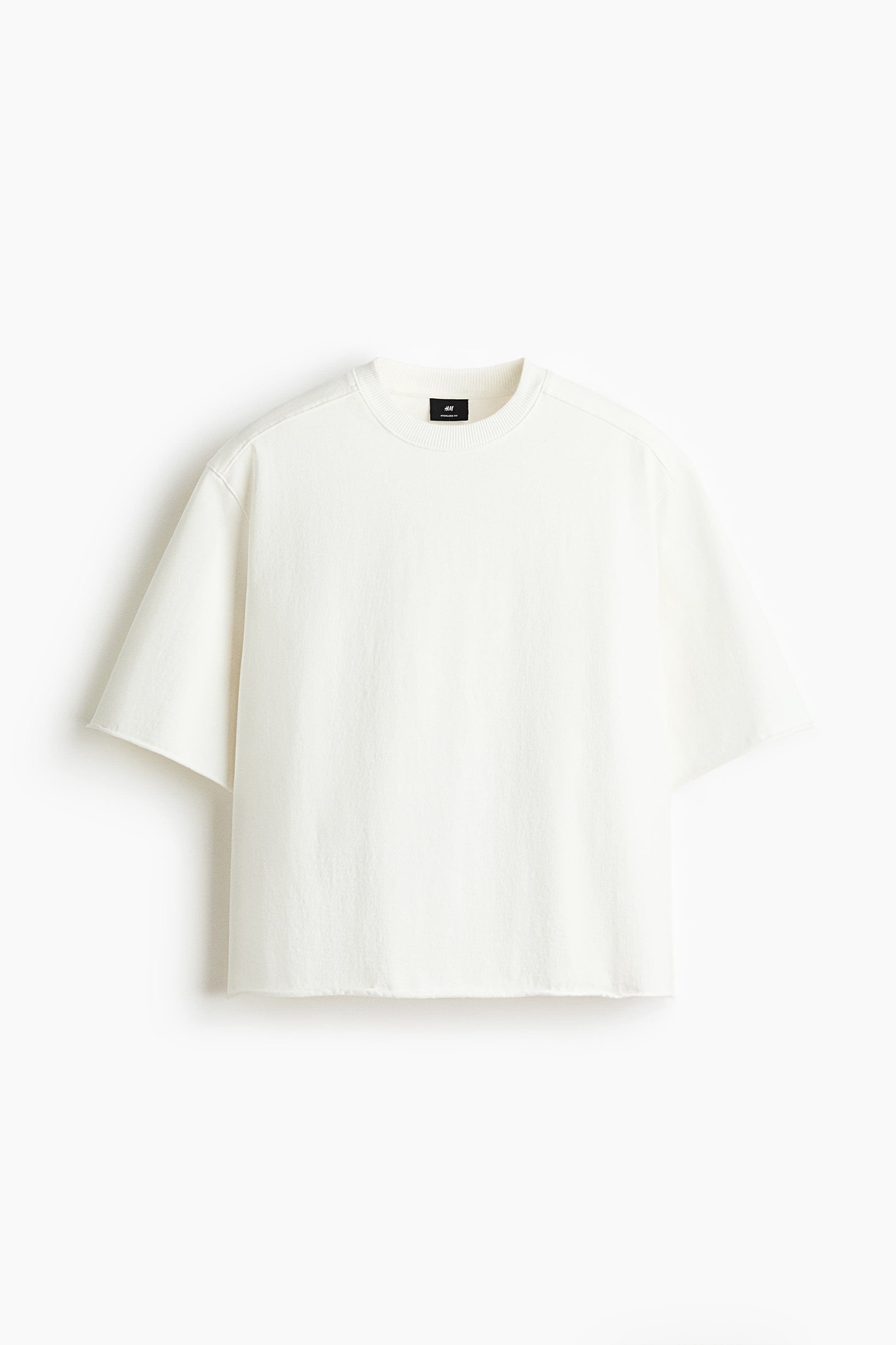 View larger image: A heavyweight off-white T-shirt is shown from the front, featuring an oversized, boxy fit with a round, rib-trimmed neckline, dropped shoulders, and visible yokes at the front and back. Raw edges finish the cuffs and hem.