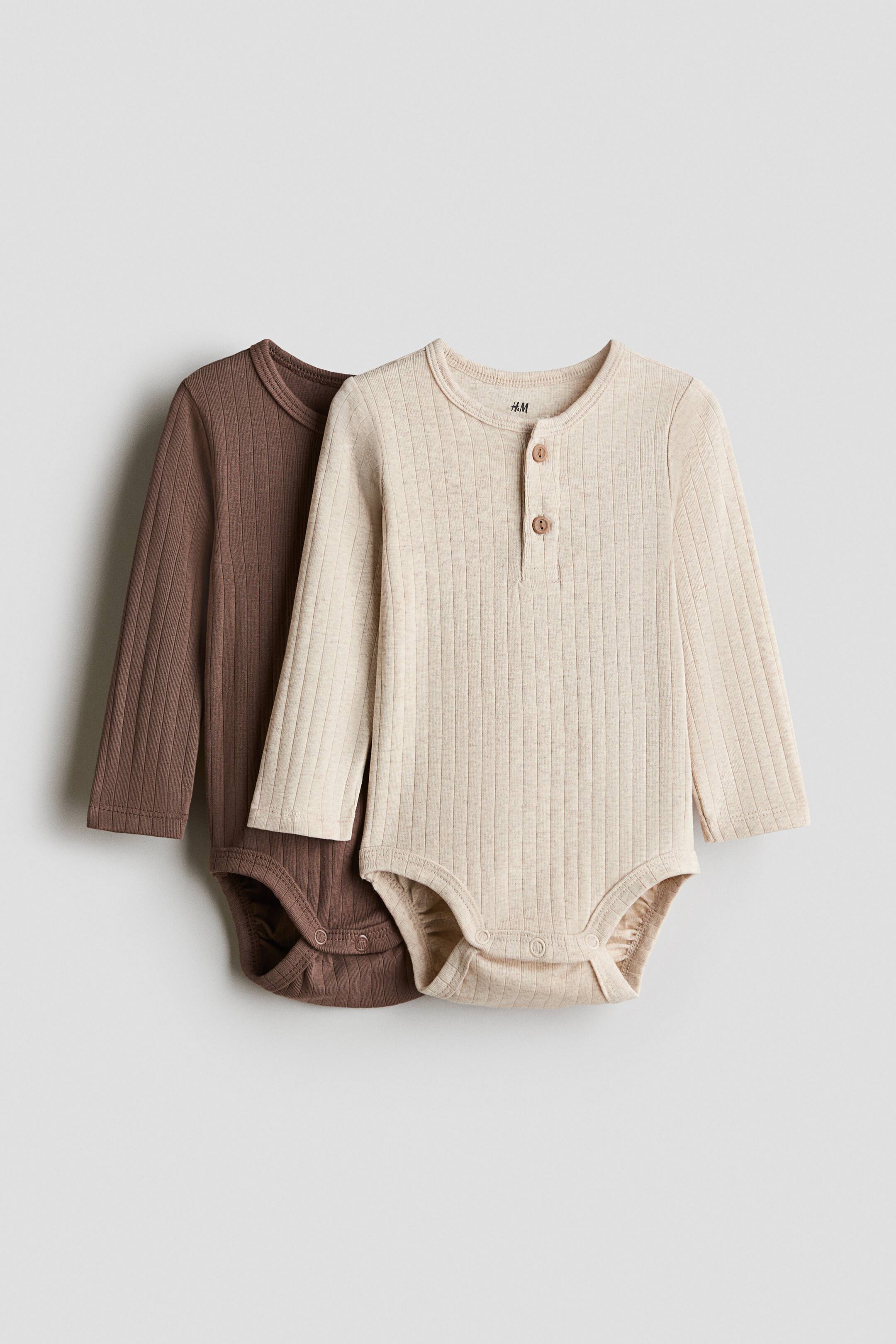 View larger image: Two ribbed cotton jersey Henley-style bodysuits, one in light beige and one in brown, are presented from the front. Both bodysuits feature a round neckline, a button placket, long sleeves, and press studs at the bottom.