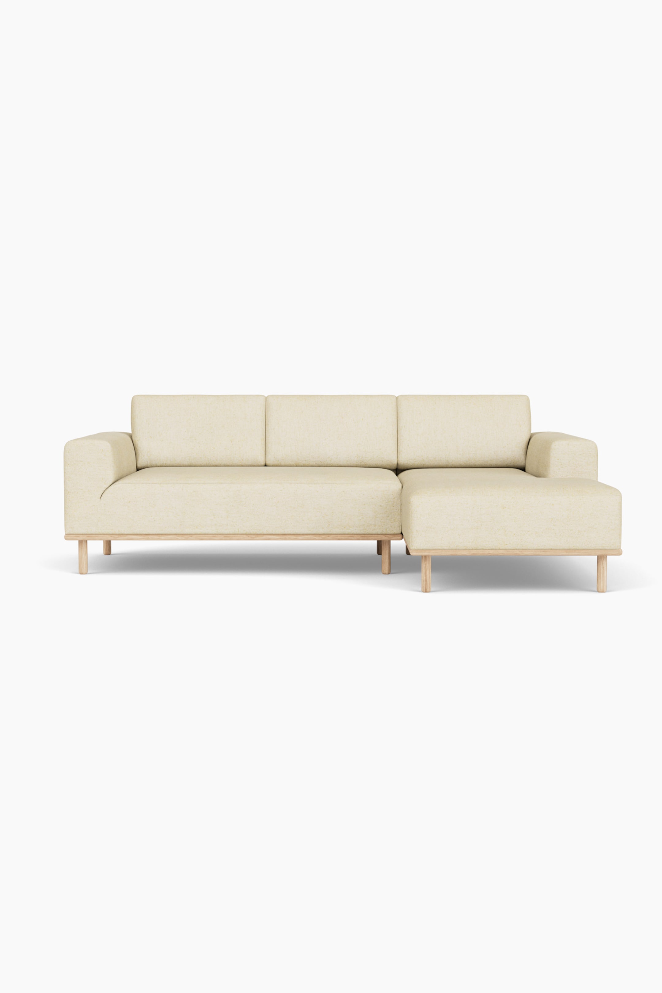 Größeres Bild ansehen: Ein frontal aufgenommenes Ecksofa, bezogen mit einem hellbeigen, strukturierten Stoff, ruht auf einem hellen Holzsockel mit runden, konisch zulaufenden Beinen. Das Sofa verfügt über eine rechts angeordnete Chaiselongue, drei rechteckige Rückenkissen und niedrige, kantige Armlehnen.