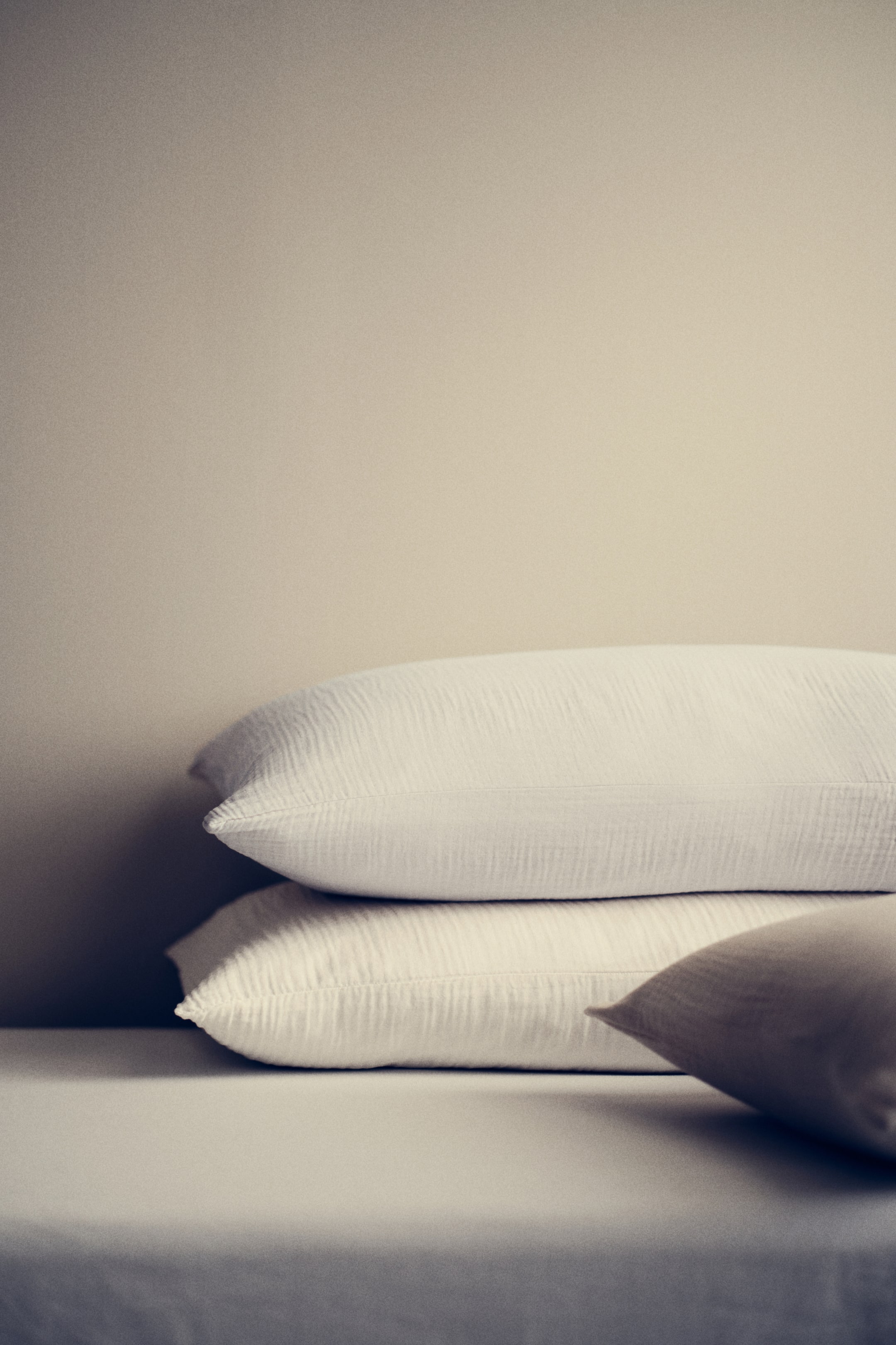 Ingrandisci l'immagine: Cuscini: Due cuscini color crema con una texture increspata simile alla garza sono impilati orizzontalmente, mentre un terzo cuscino, leggermente più scuro di colore beige, è posizionato a destra, inclinato verso l'osservatore.