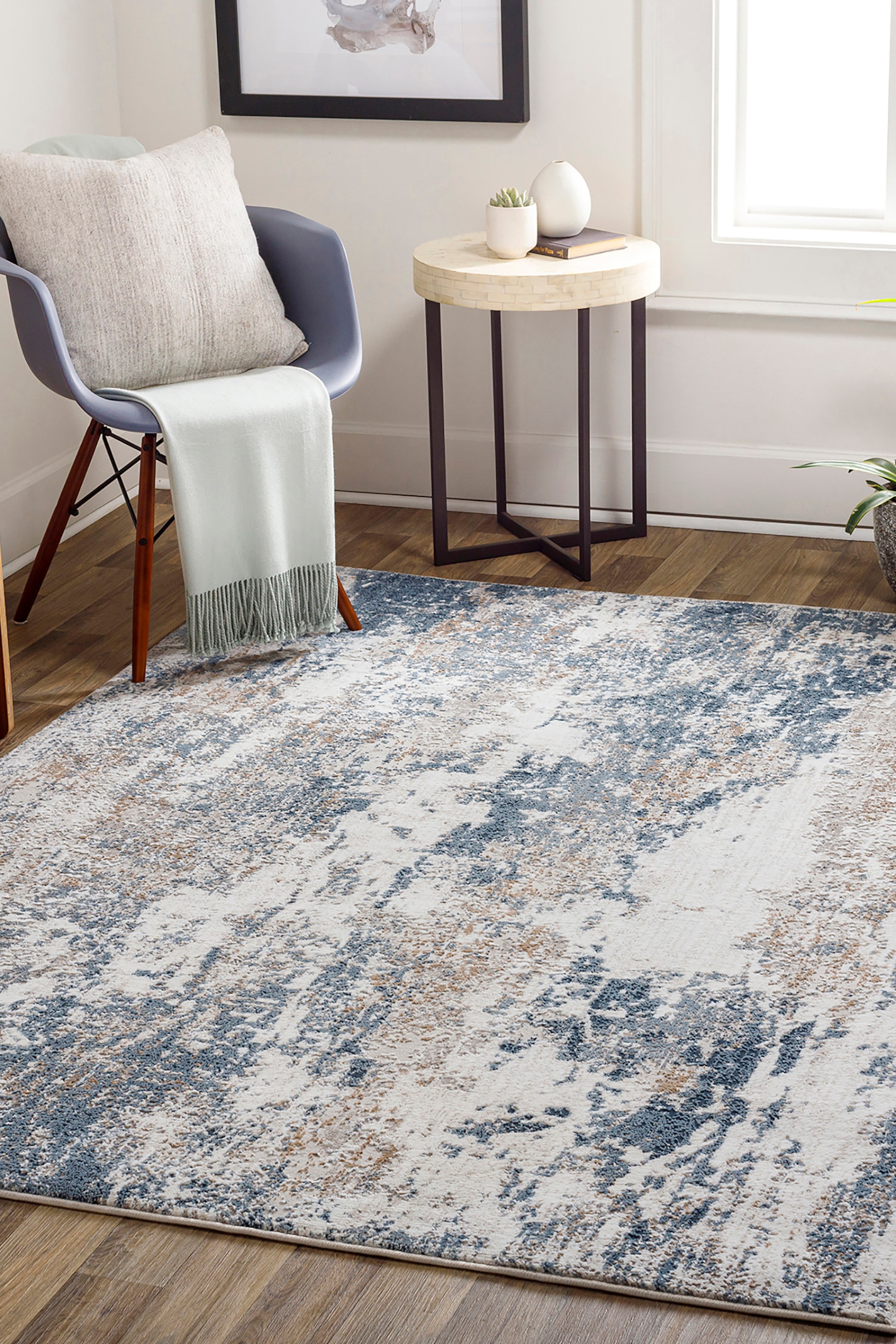 View larger image: A rectangular area rug is displaying a distressed, abstract pattern with splashes of slate blue and beige over a cream-coloured base. The low-pile rug is showcasing a textured weave and clean, bound edges.