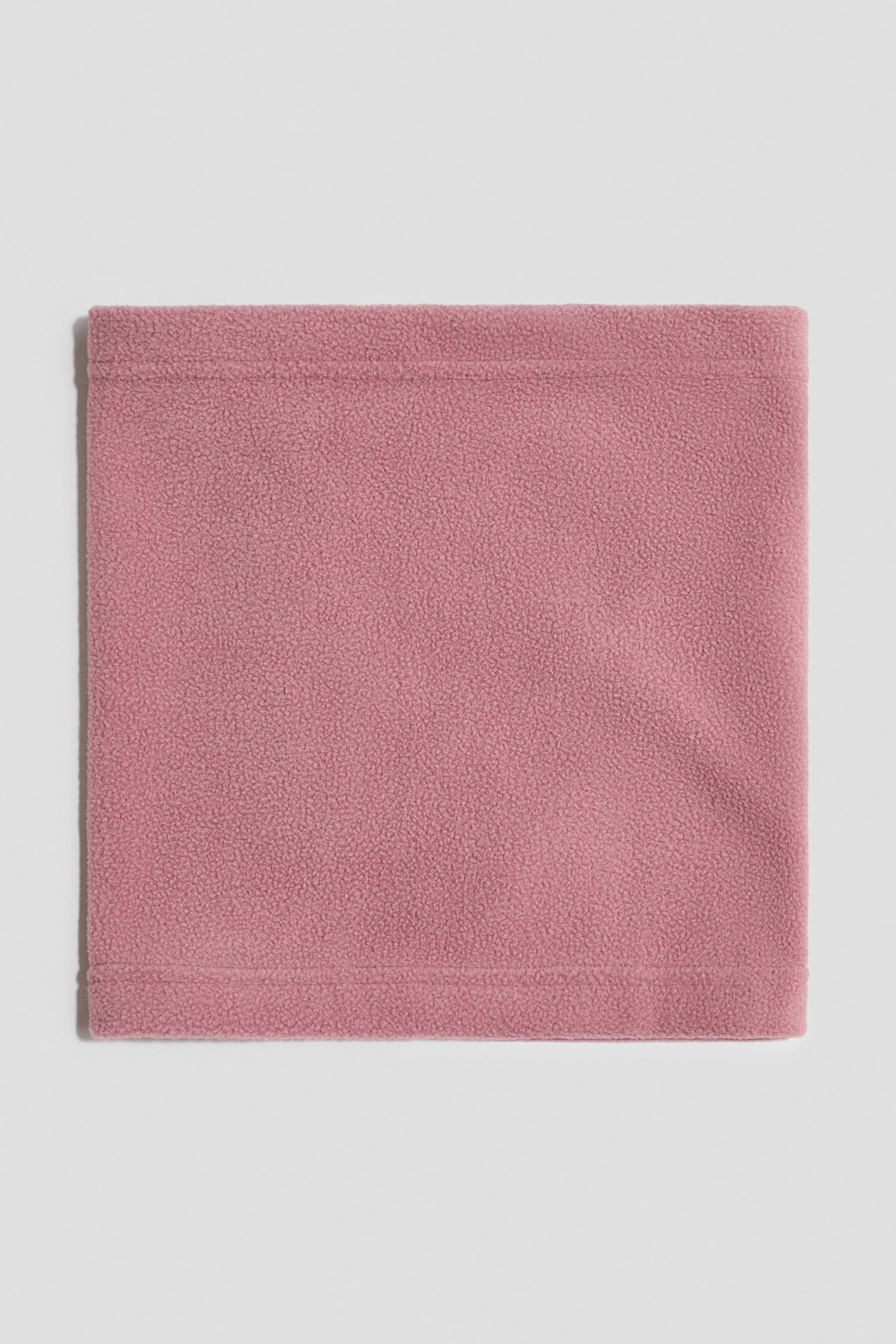 Una bufanda tubular de tela polar rosa empolvado estÃ¡ colocada plana, mostrando su forma rectangular desde el frente. Presenta dobladillos cosidos en los bordes superior e inferior, resaltando el material polar suave y texturizado.