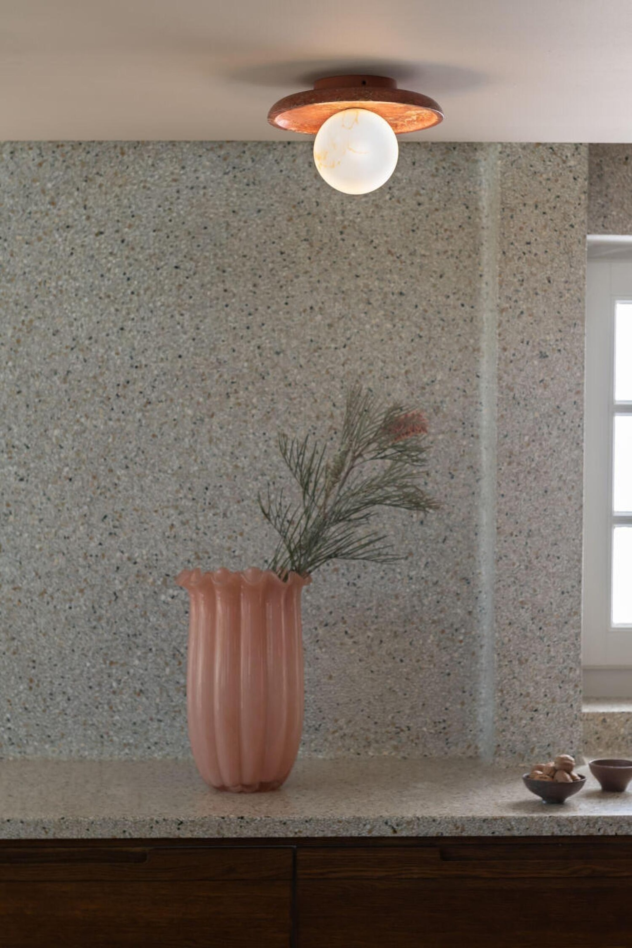 Grotere afbeelding bekijken: Een plafondlamp voor opbouwmontage met een getextureerde, ondiepe koepelvormige kap in koperen kleur en een lichtgevende, bolvormige witte glazen bol die centraal hangt.