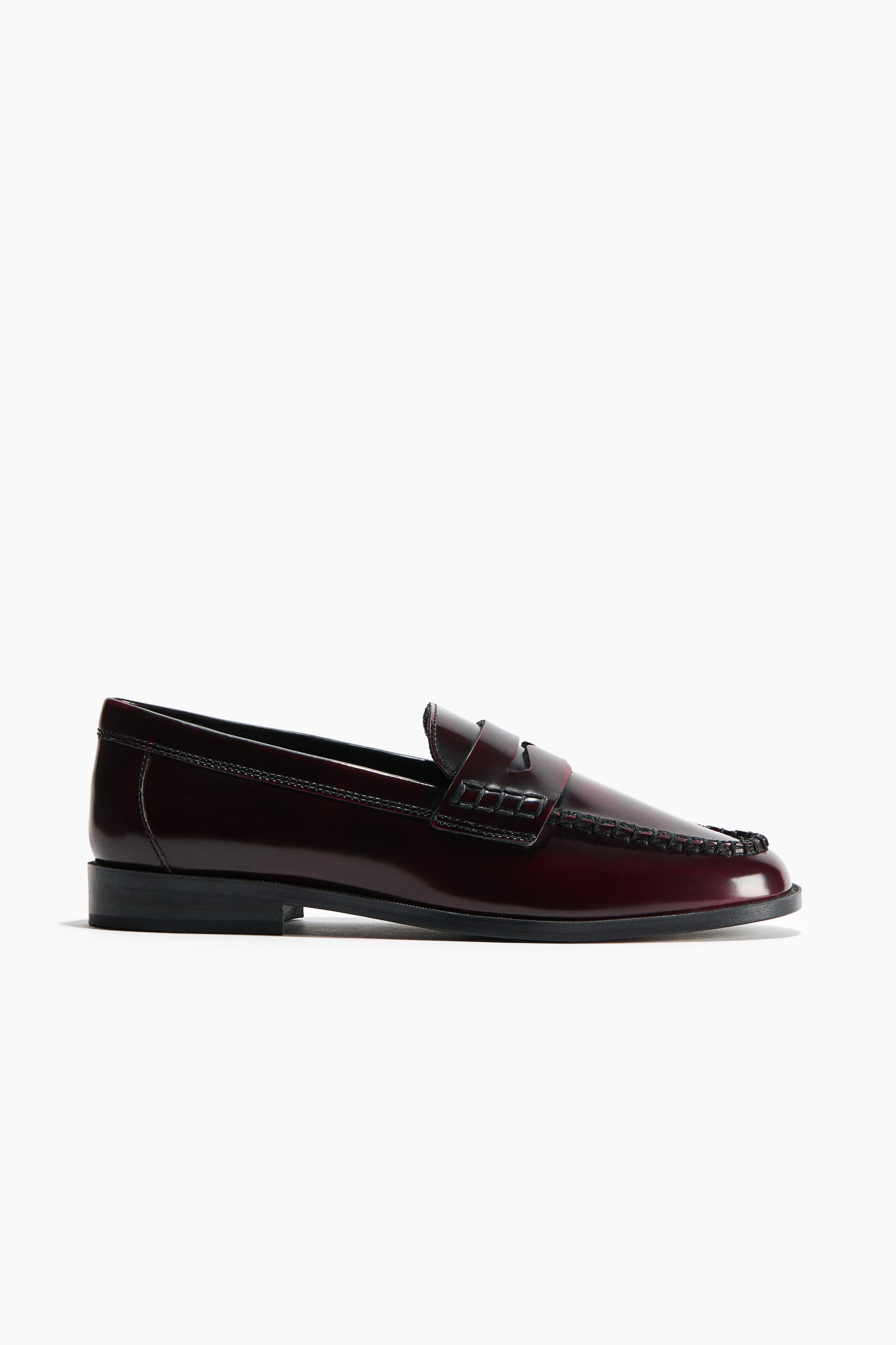 View larger image: A polished burgundy leather loafer is shown in side profile, facing right, featuring a prominent stitched moccasin seam around the toe and a classic penny keeper strap across the vamp.