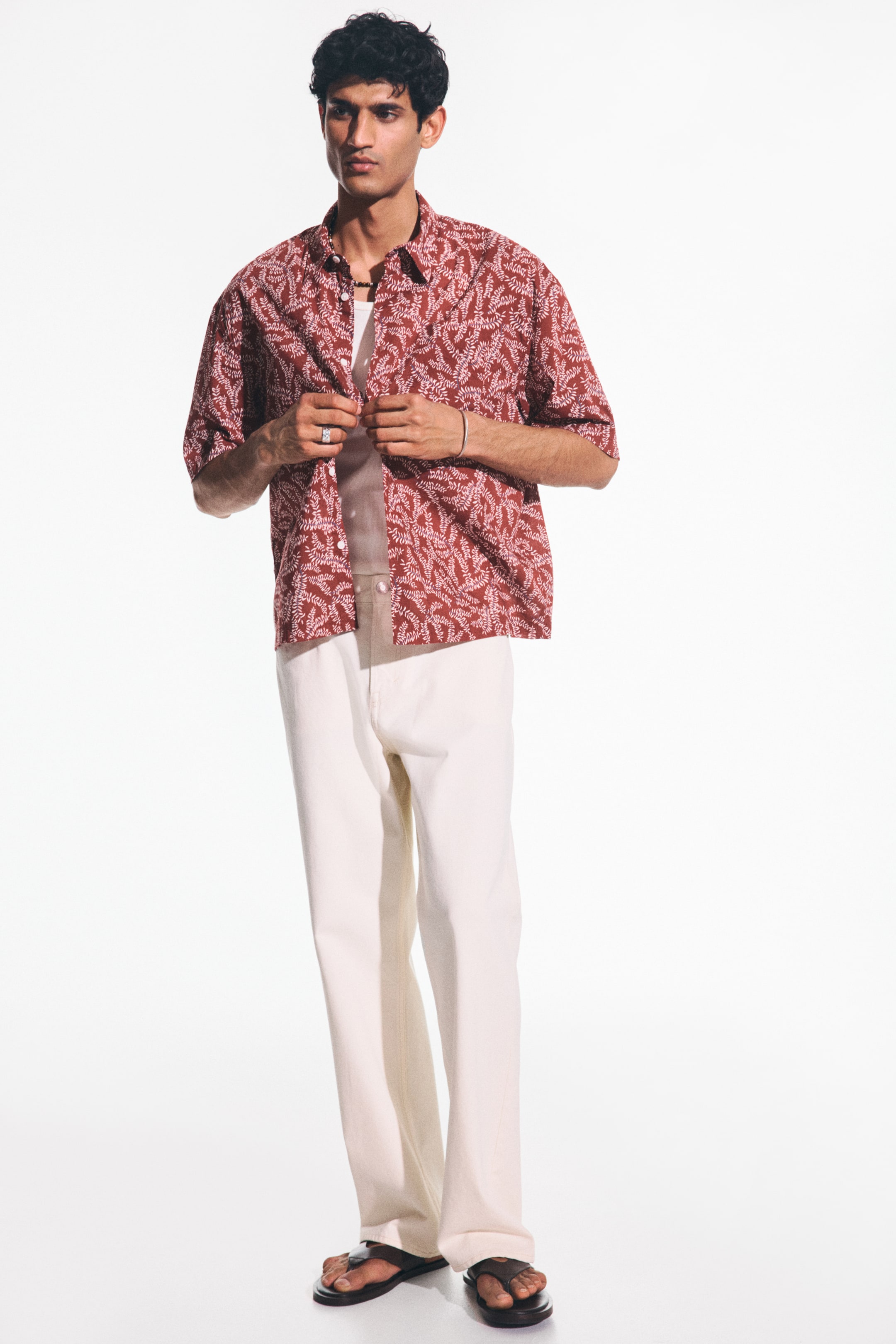 View larger image: A red short-sleeved shirt, adorned with white leaf-like motifs, is styled with its front open, showcasing a light-hued undershirt. The shirt boasts a spread collar and a relaxed fit.