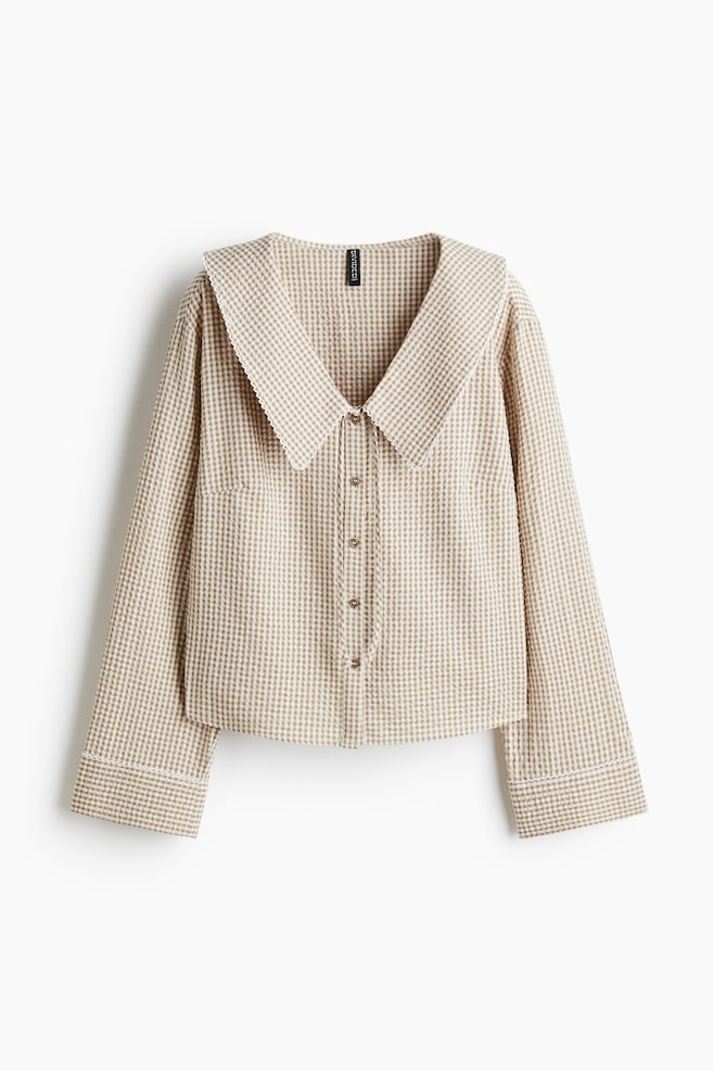 A light beige and white gingham shirt is presented from the FRONT, featuring an oversized pointed collar with a white scalloped trim. It is designed with a button-front closure, long wide sleeves with matching scalloped cuffs, and a single patch pocket on the left chest. - 1