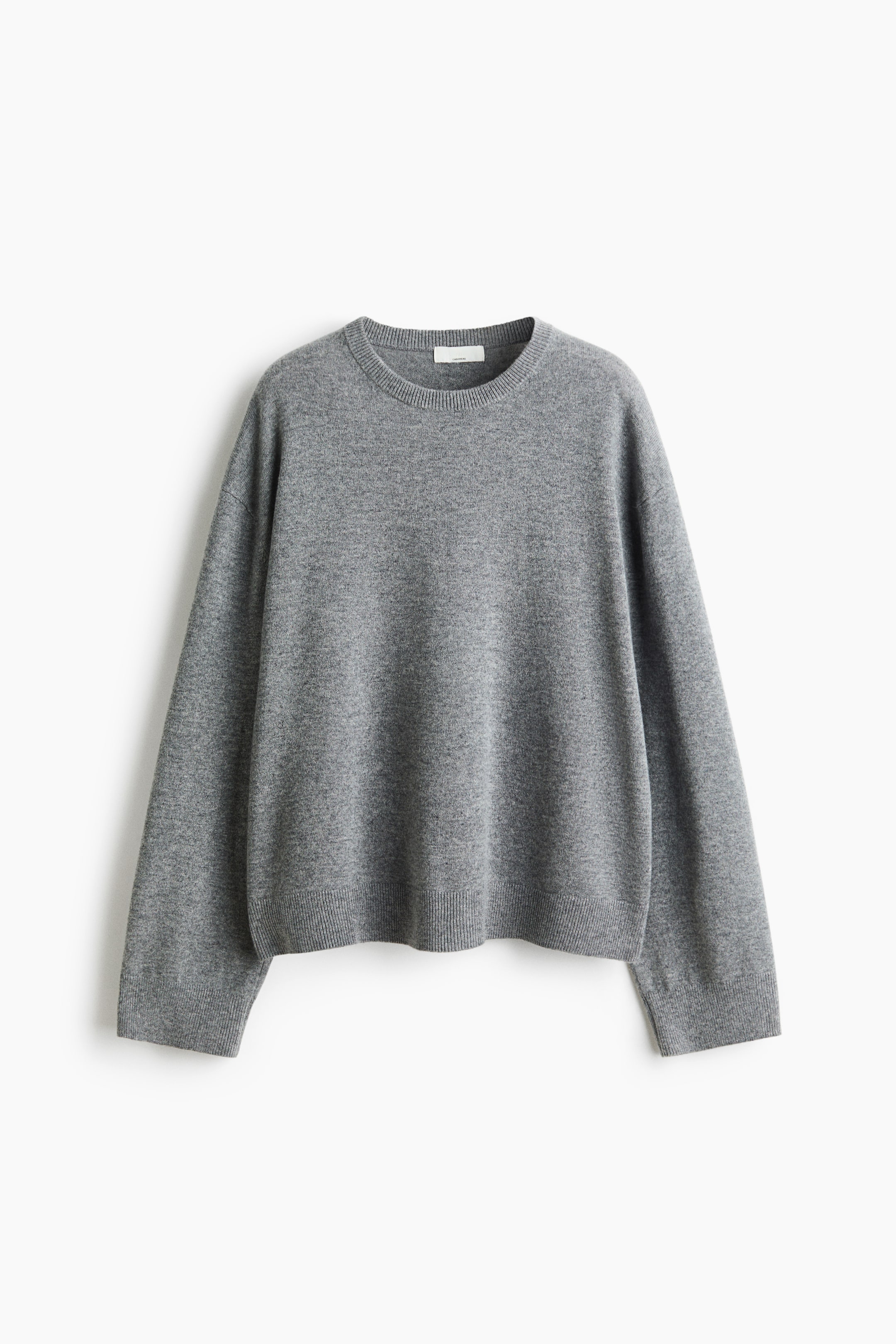 View larger image: A relaxed-fit, grey cashmere sweater is shown from the front, featuring a round, rib-trimmed neckline, low dropped shoulders, and long sleeves. The sweater is designed with ribbed cuffs and a matching ribbed hem.