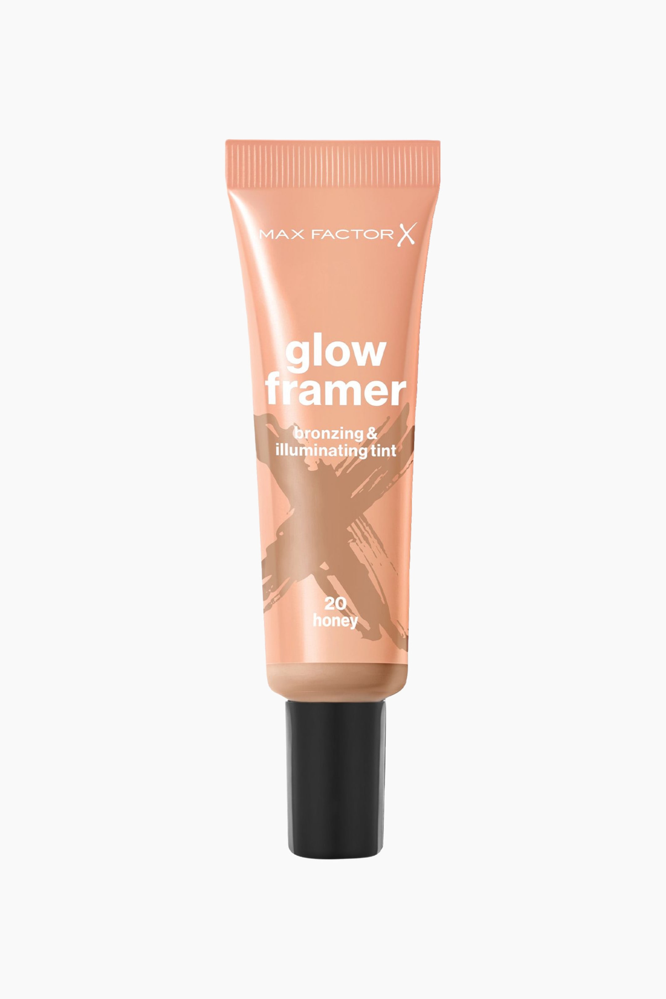 Visa större bild: Ett persikofärgat-bronsigt metalliskt kosmetiskt klämtub står upprätt och visar "MAX FACTOR X glow framer bronzing & illuminating tint" med en mörkbronsig penseldrag "X"-grafik över dess mitt. Tuben visar också nyansen "20 honey" vid dess bas, som är förseglad med en svart kork.