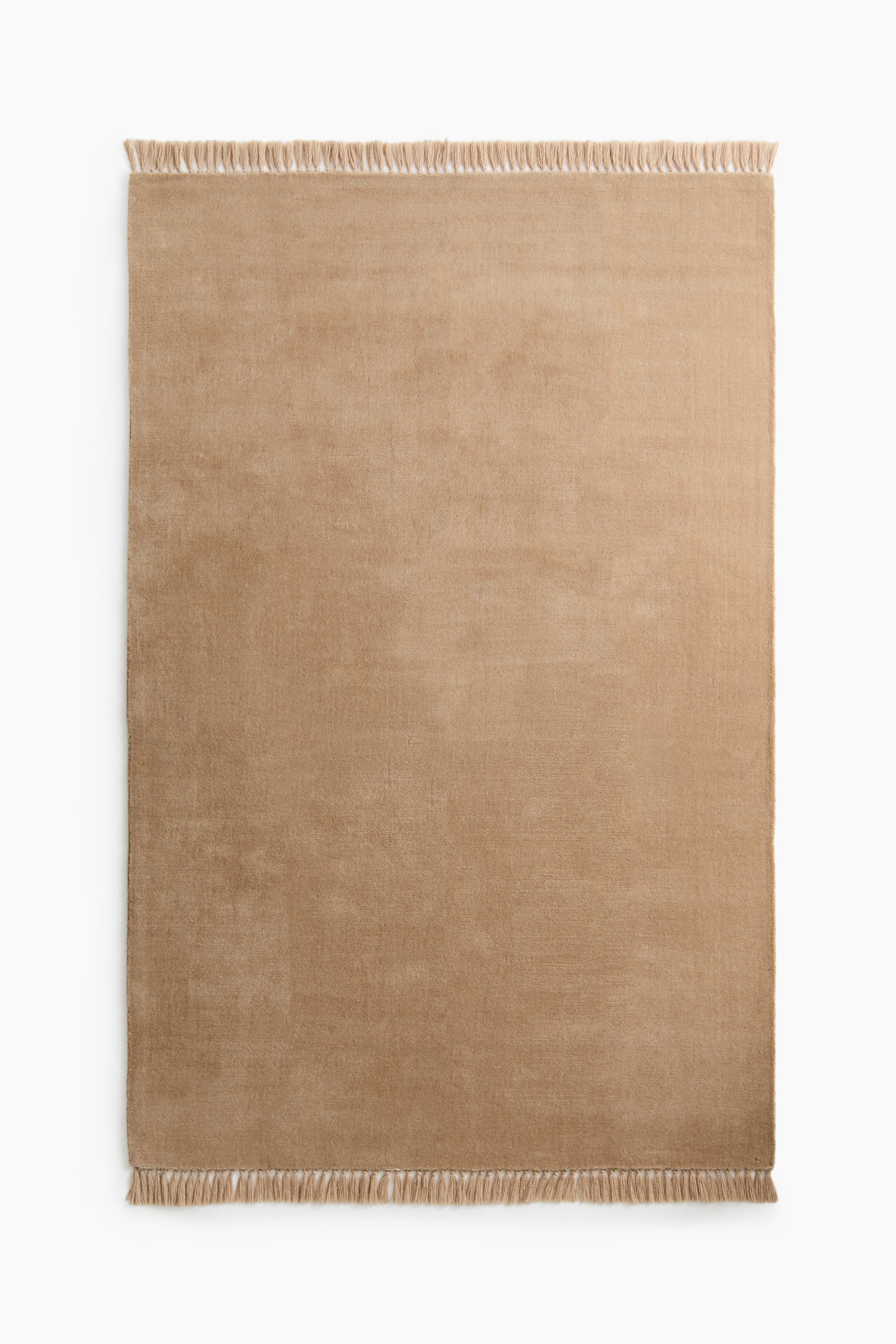 View larger image: A tan rectangular rug is lying flat, showcasing a smooth pile surface. It features fringed ends on its top and bottom sides.