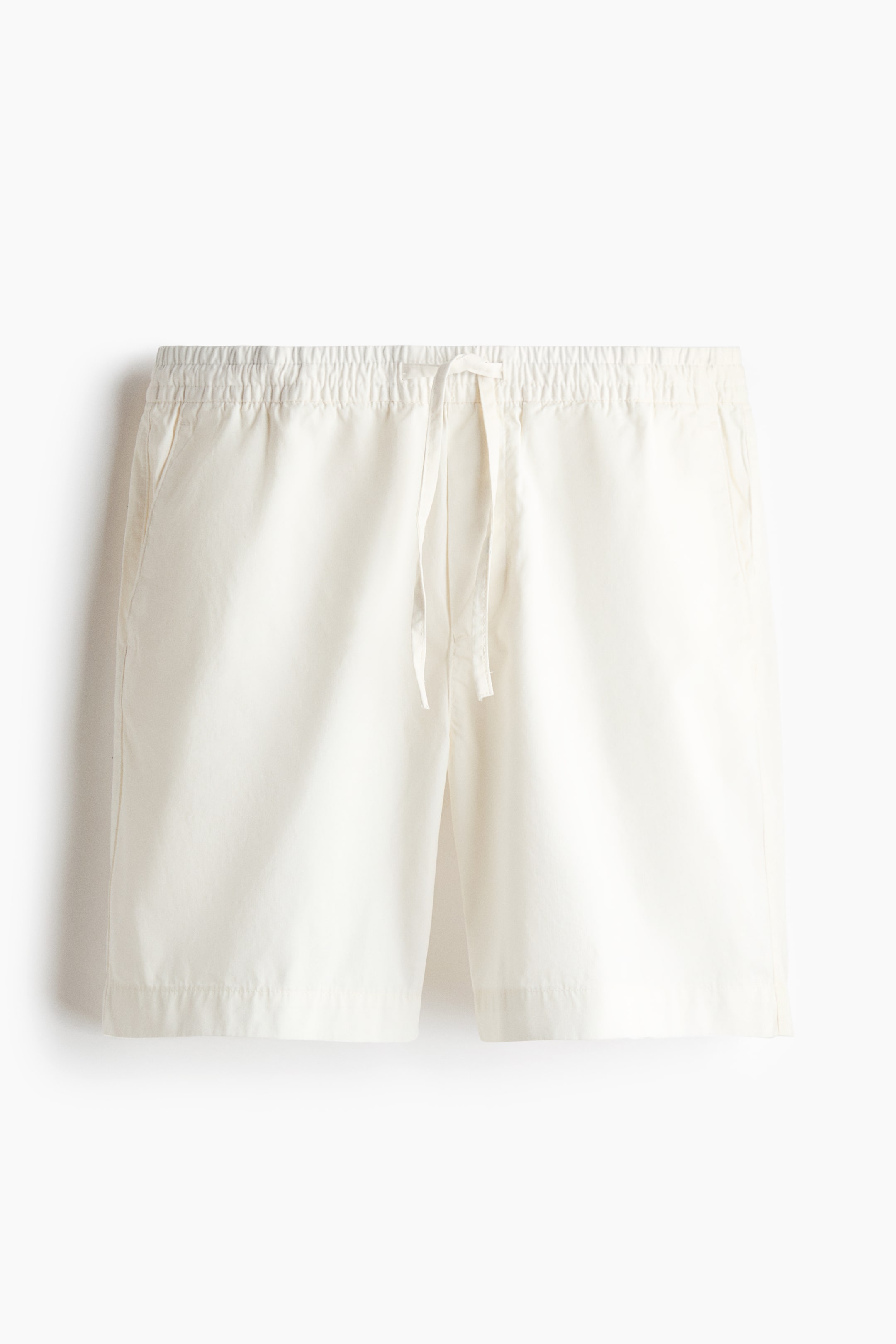 View larger image: Off-white shorts are shown from the front, featuring an elastic drawstring waist and diagonal side pockets. The shorts have a relaxed fit.