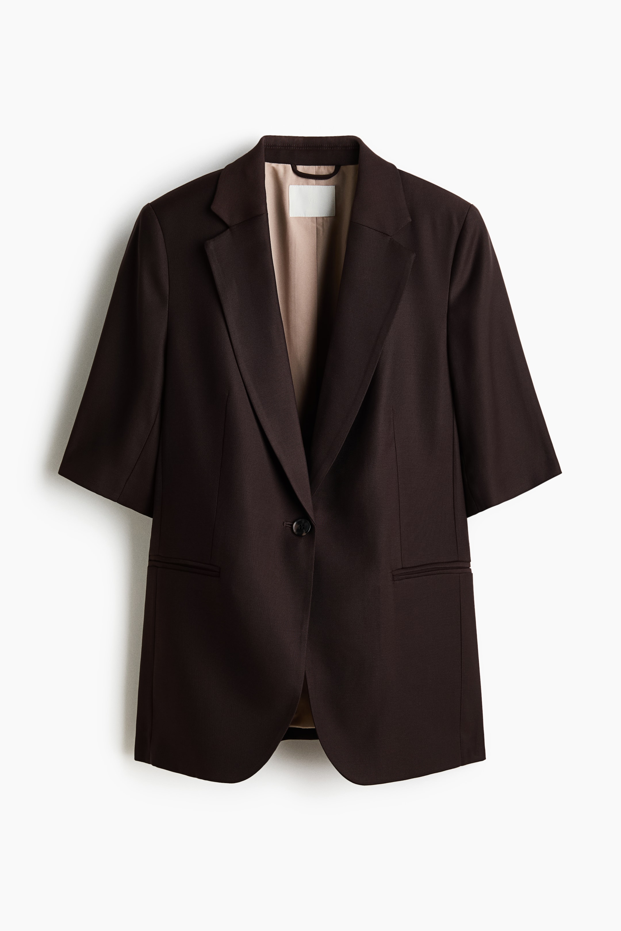 Grotere afbeelding bekijken: Een donkerbruine blazer is aan de voorkant te zien, met ellebooglange mouwen, inkepingsrevers en een enkele knoopsluiting. Twee klepzakken zijn zichtbaar aan de voorkant en een lichtbeige voering is te zien in de opening.