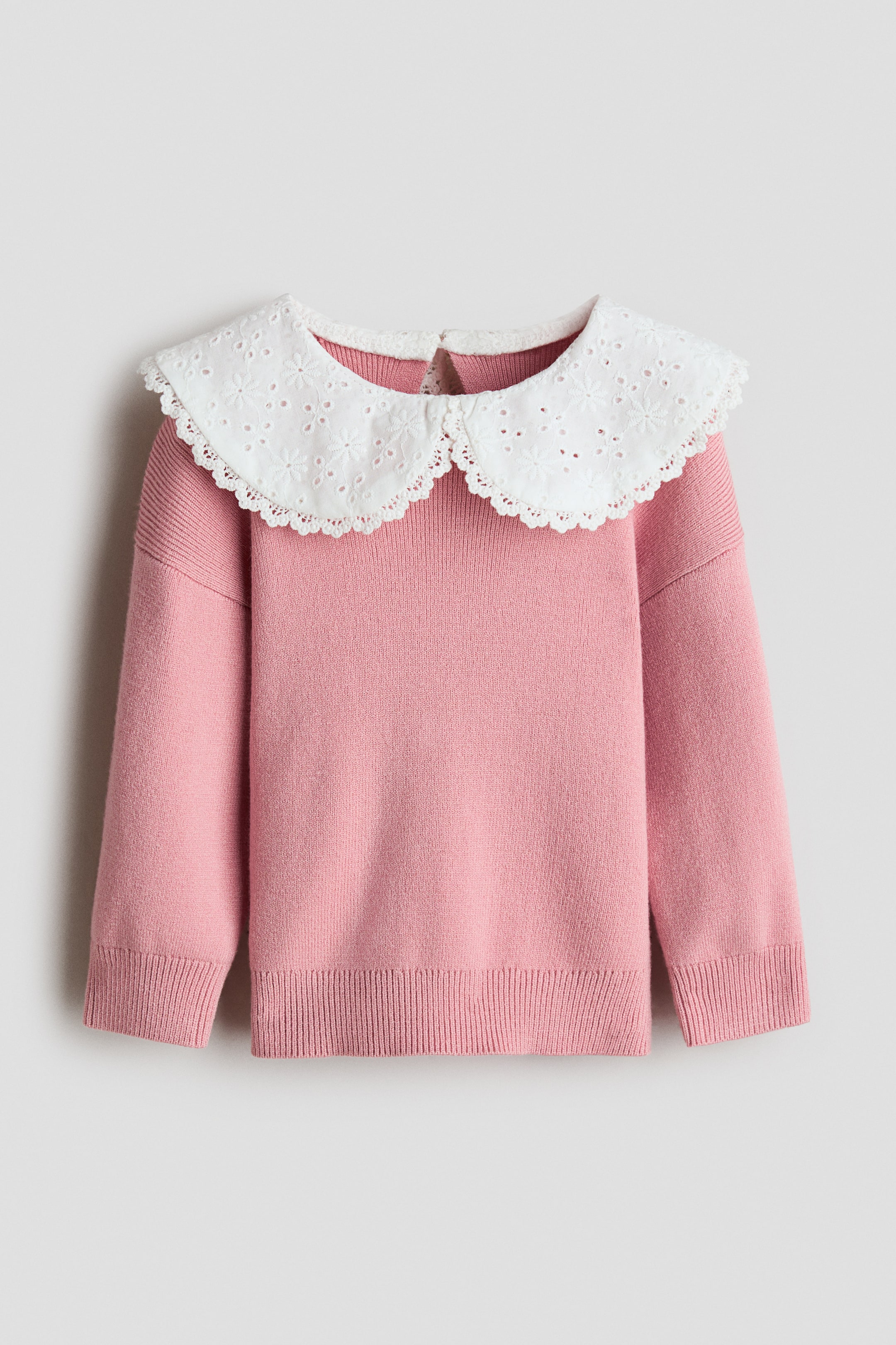 Größeres Bild anzeigen: Ein rosa Pullover wird von vorne gezeigt und verfügt über einen kontrastierenden weißen, abgerundeten Kragen mit Lochstickerei und gewelltem Saum, der über den Halsausschnitt gelegt ist. Außerdem sind lange Ärmel, Rippbündchen und ein gerippter Saum zu sehen.