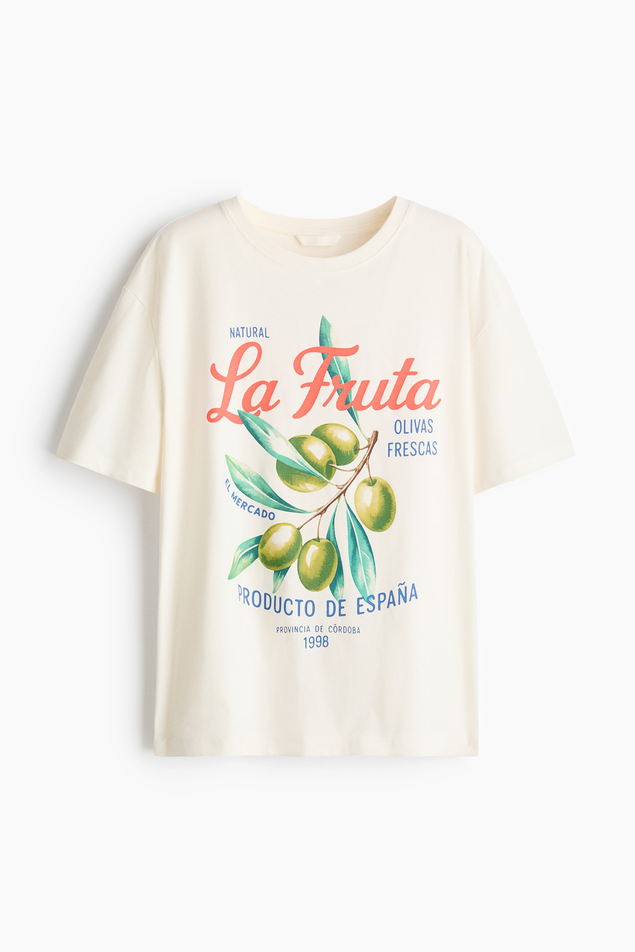 Visa större bild: En krämfärgad t-shirt ligger platt och visar en avslappnad passform med korta ärmar och en ribbad rund hals. På framsidan visas ett grafiskt tryck av en olivkvist med gröna oliver och blad, tillsammans med texten "La Fruta" i röd skrivstil och "Natural," "Olivas Frescas," "El Mercado," "Producto de España," "Provincia de Córdoba," och "1998" i blå och svart text.