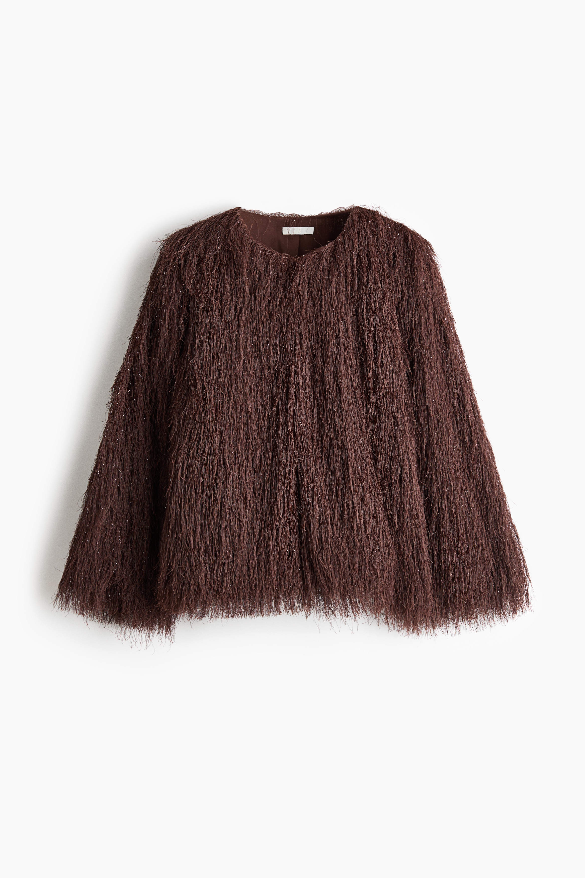 A dark brown, loose-fit jacket covered in textured, long fringes with subtle metallic flecks is being worn by the model. The jacket features a round neckline and is layered over a black turtleneck top and black leather trousers.