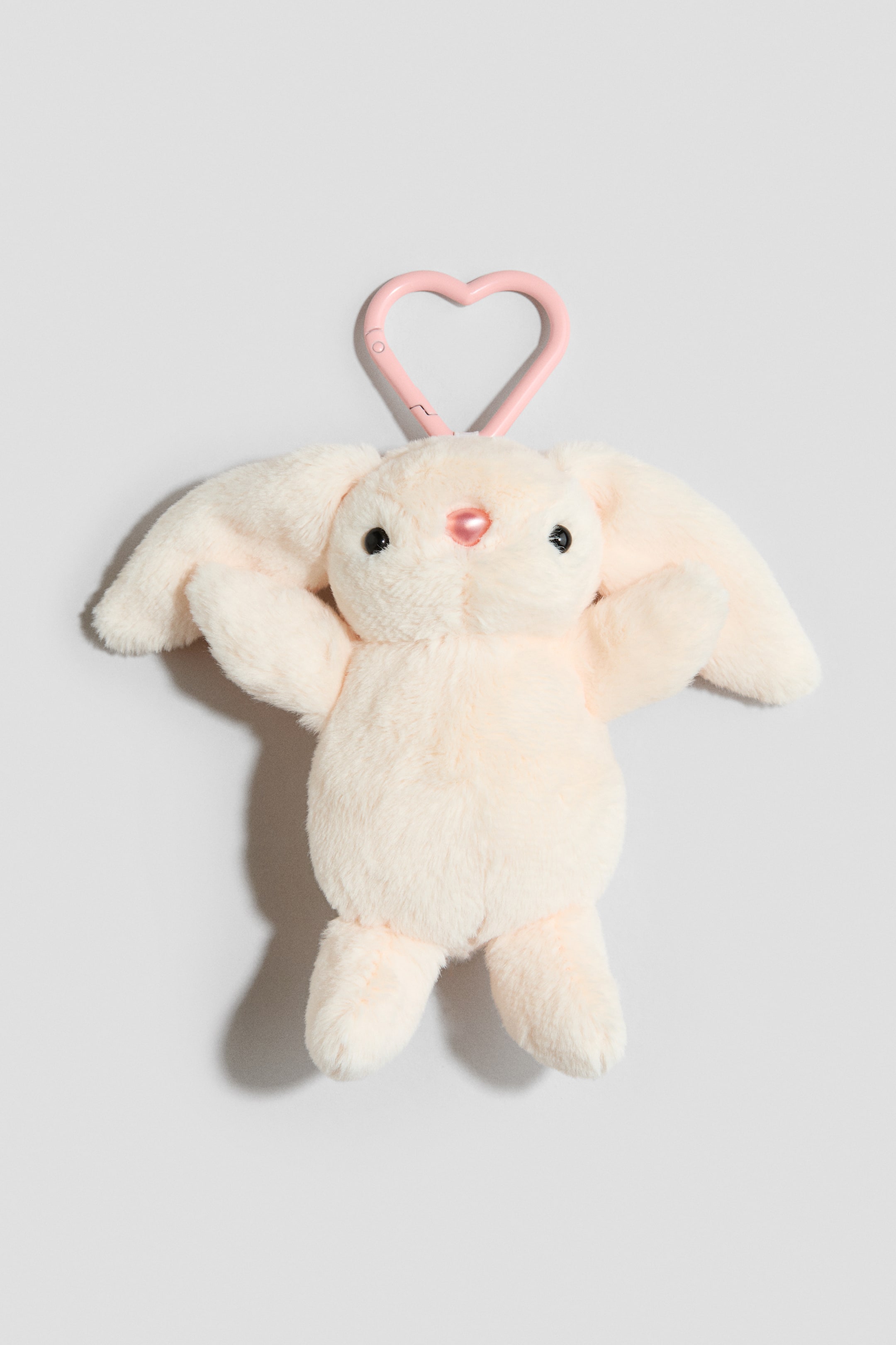 View larger image: The bag charm showcases a large, padded soft toy bunny with black eyes, a pink nose, and floppy ears, facing FRONT, attached to a pink heart-shaped metal carabiner hook.