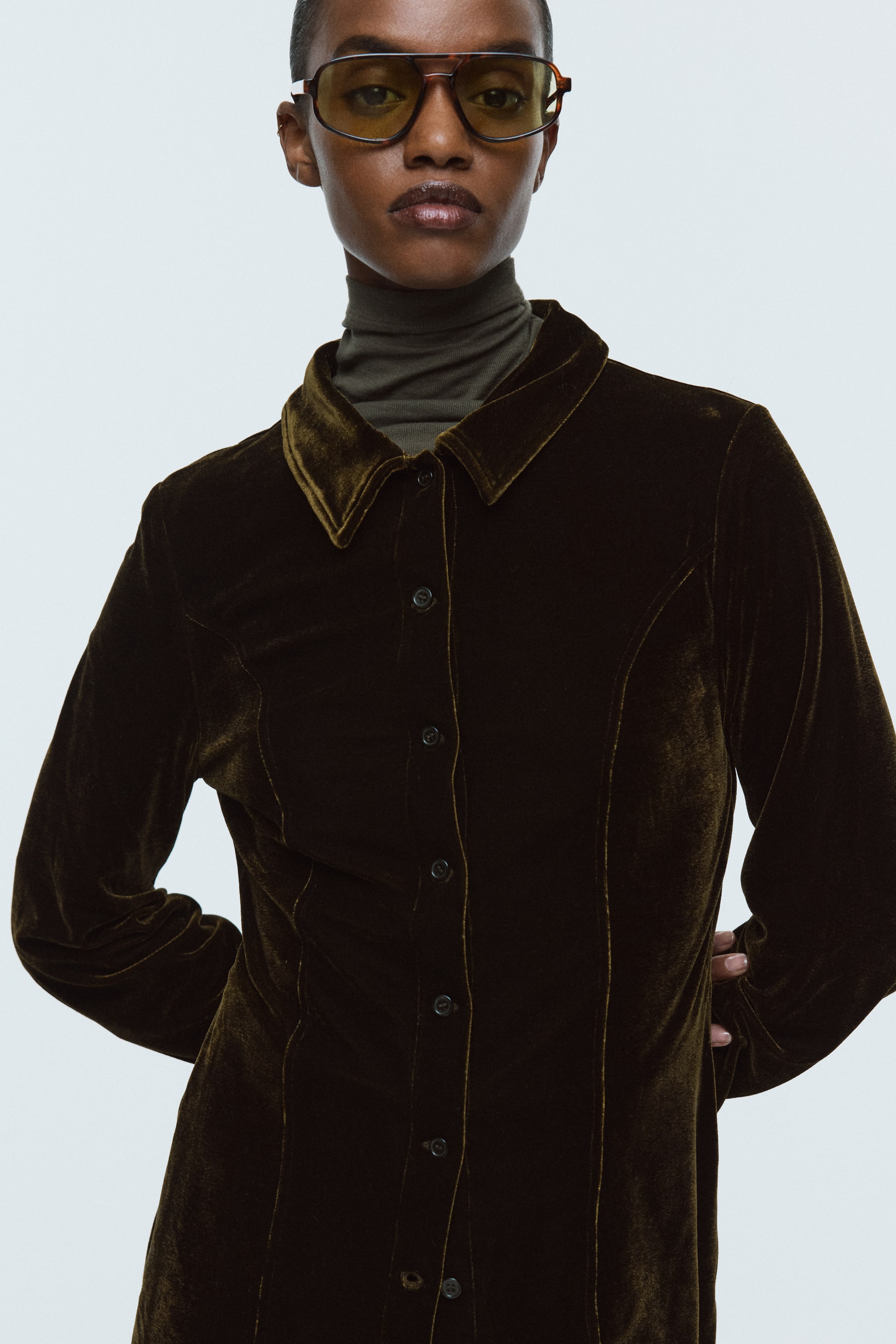 View larger image: A dark olive velvet shirt is featuring a pointed collar, a full button placket down the front, and long sleeves, seen from the front. Visible vertical seams are shaping the torso, and a dark green turtleneck is layering underneath the shirt.