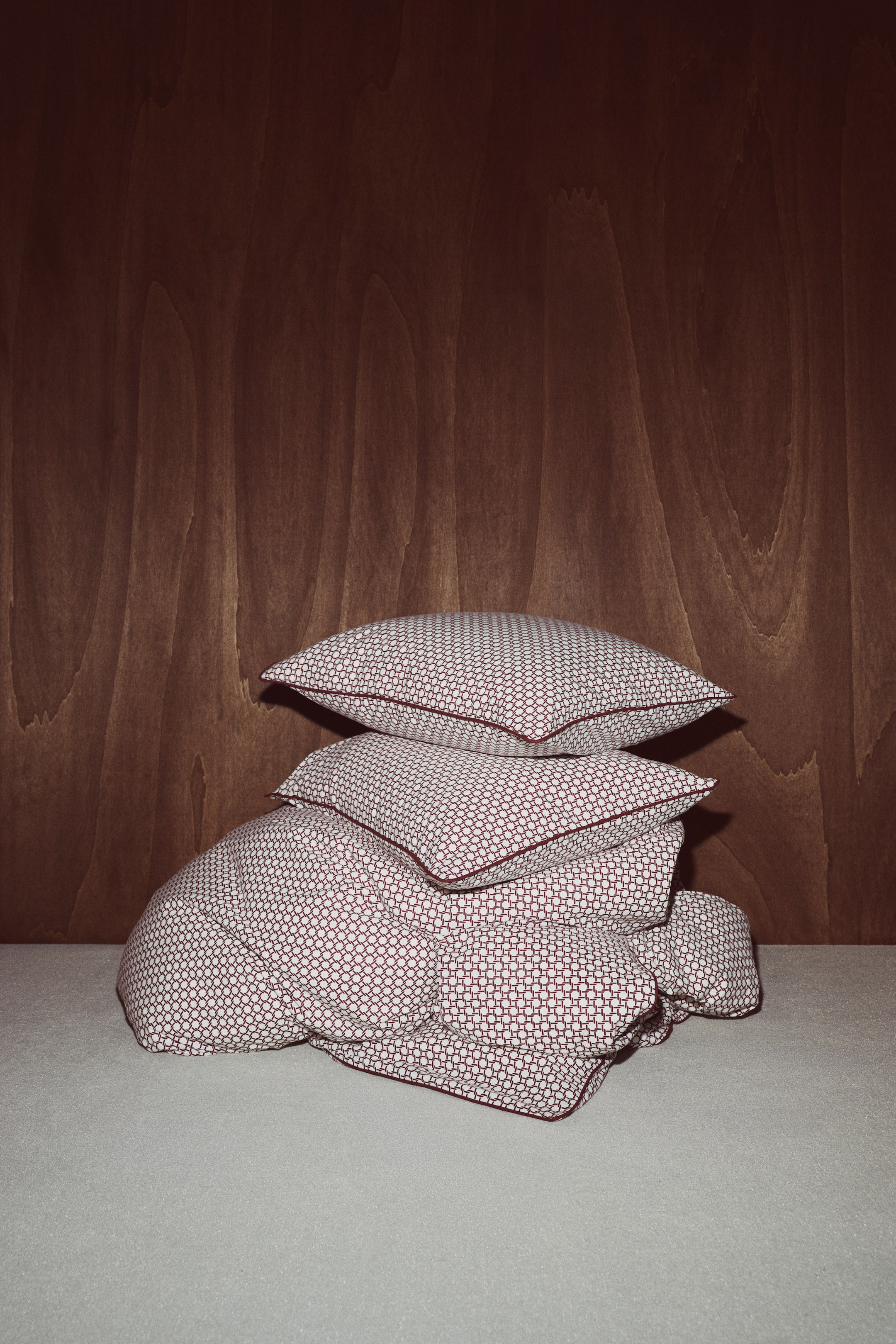 Agrandir l'image: Un ensemble de housse de couette présente une housse de couette pliée avec deux taies d’oreiller assorties empilées dessus, mettant en valeur un motif géométrique rouge et blanc ainsi que des bordures passepoilées rouges.