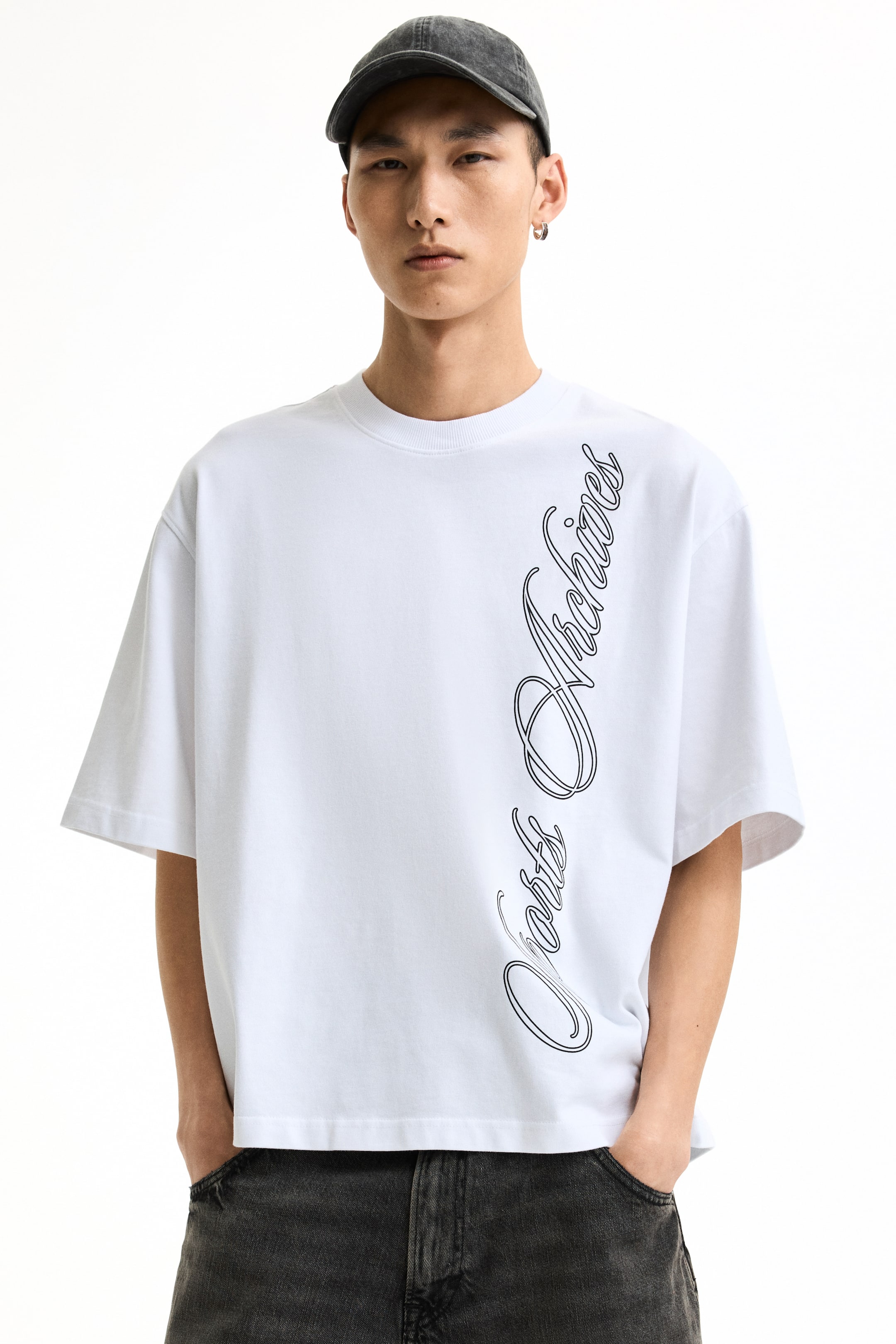 View larger image: A white oversized t-shirt is showcased front-facing, featuring a crew neck and short sleeves. A black script graphic, reading 'Ports Archives' with a double outline, runs vertically down the right side of the t-shirt, which drapes loosely over dark jeans.