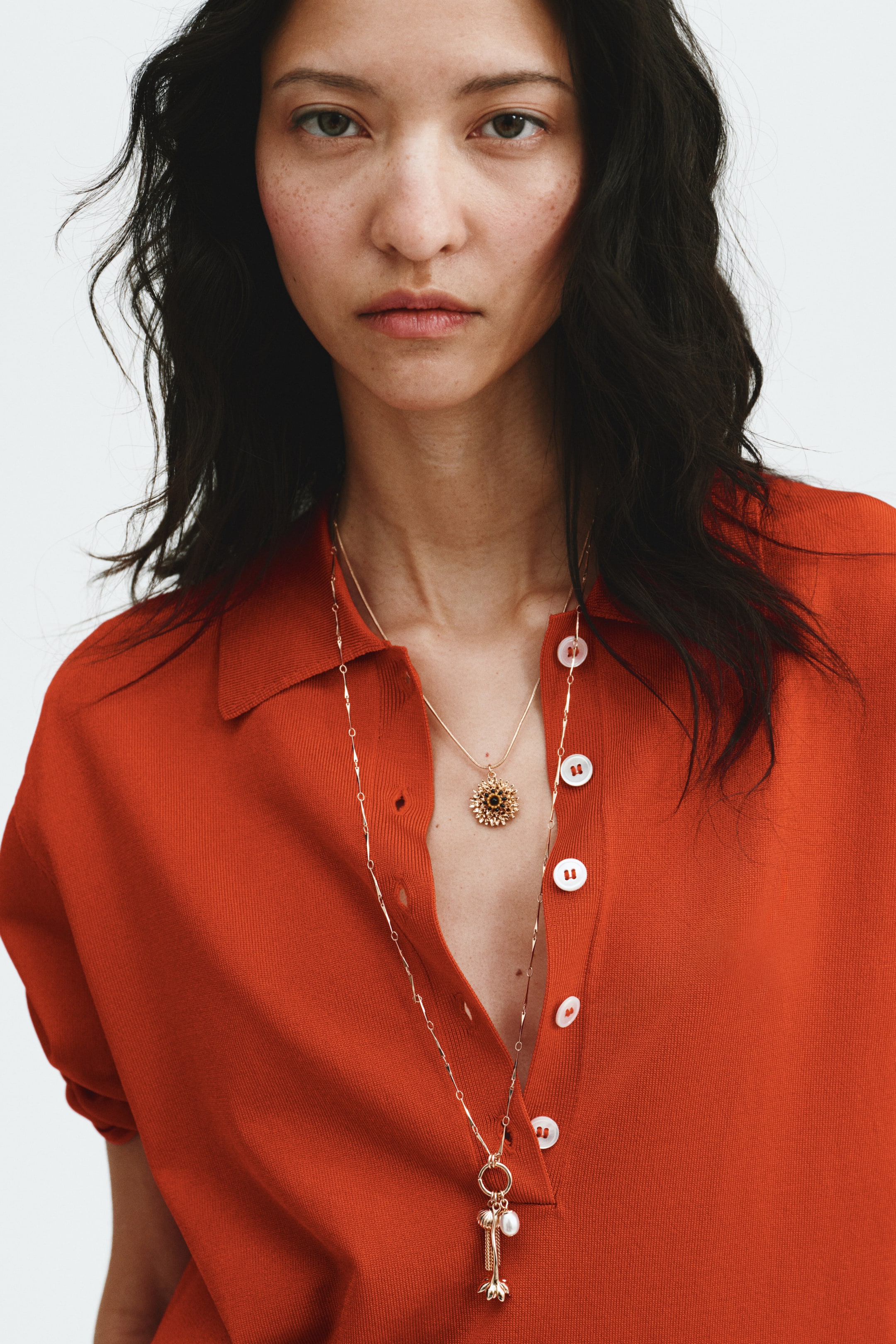 View larger image: An orange knit polo top is featuring a classic collar and a front button placket with white buttons. The top is presenting with several buttons unfastened, creating an open neckline.