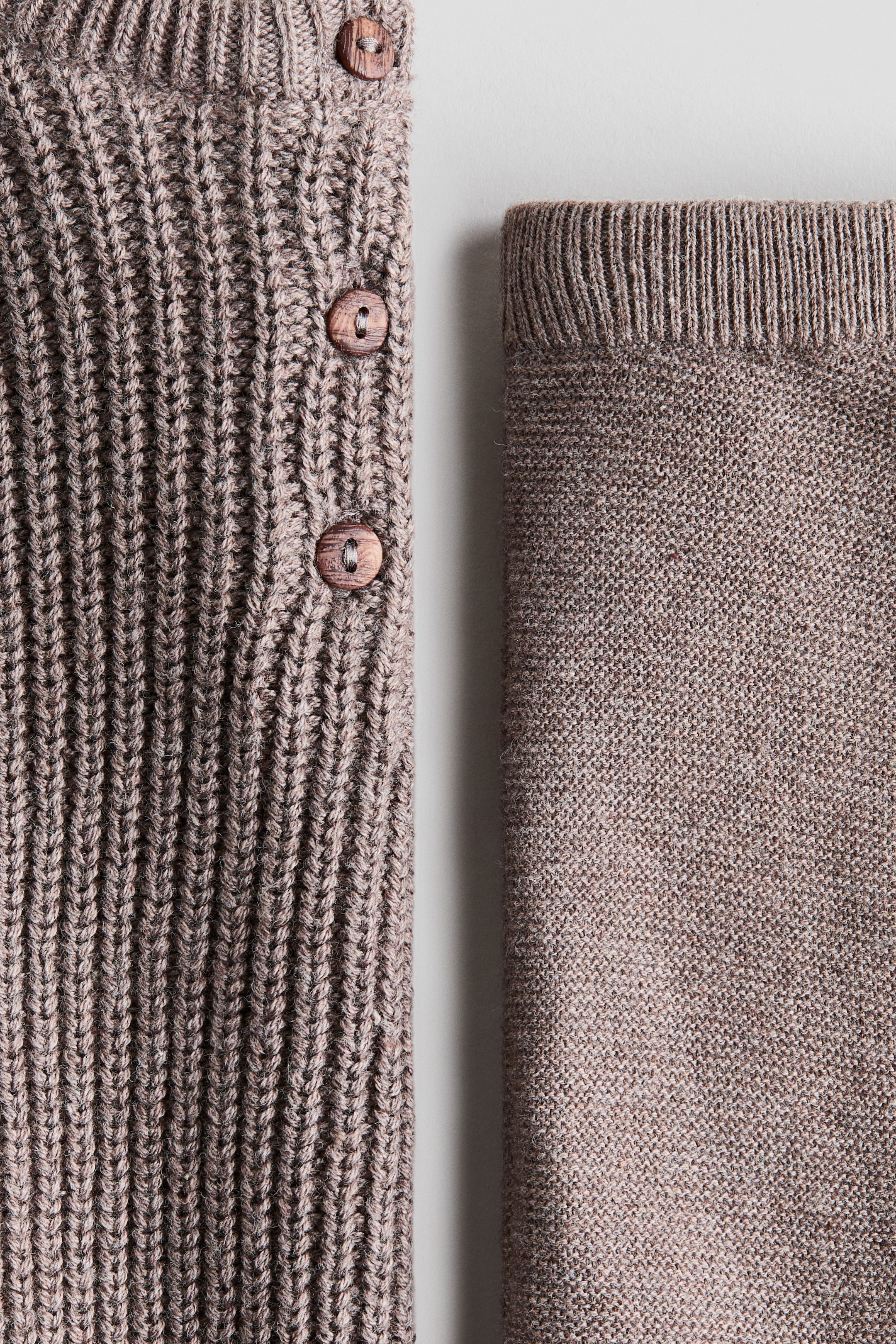 Grösseres Bild ansehen: Das H&M Adorables Set zeigt eine Nahaufnahme eines patentgestrickten Pullovers mit drei sichtbaren Holzknöpfen auf einer Seite, kombiniert mit fein gestrickten Leggings mit geripptem Bund, beide in einem sanften Braunton.