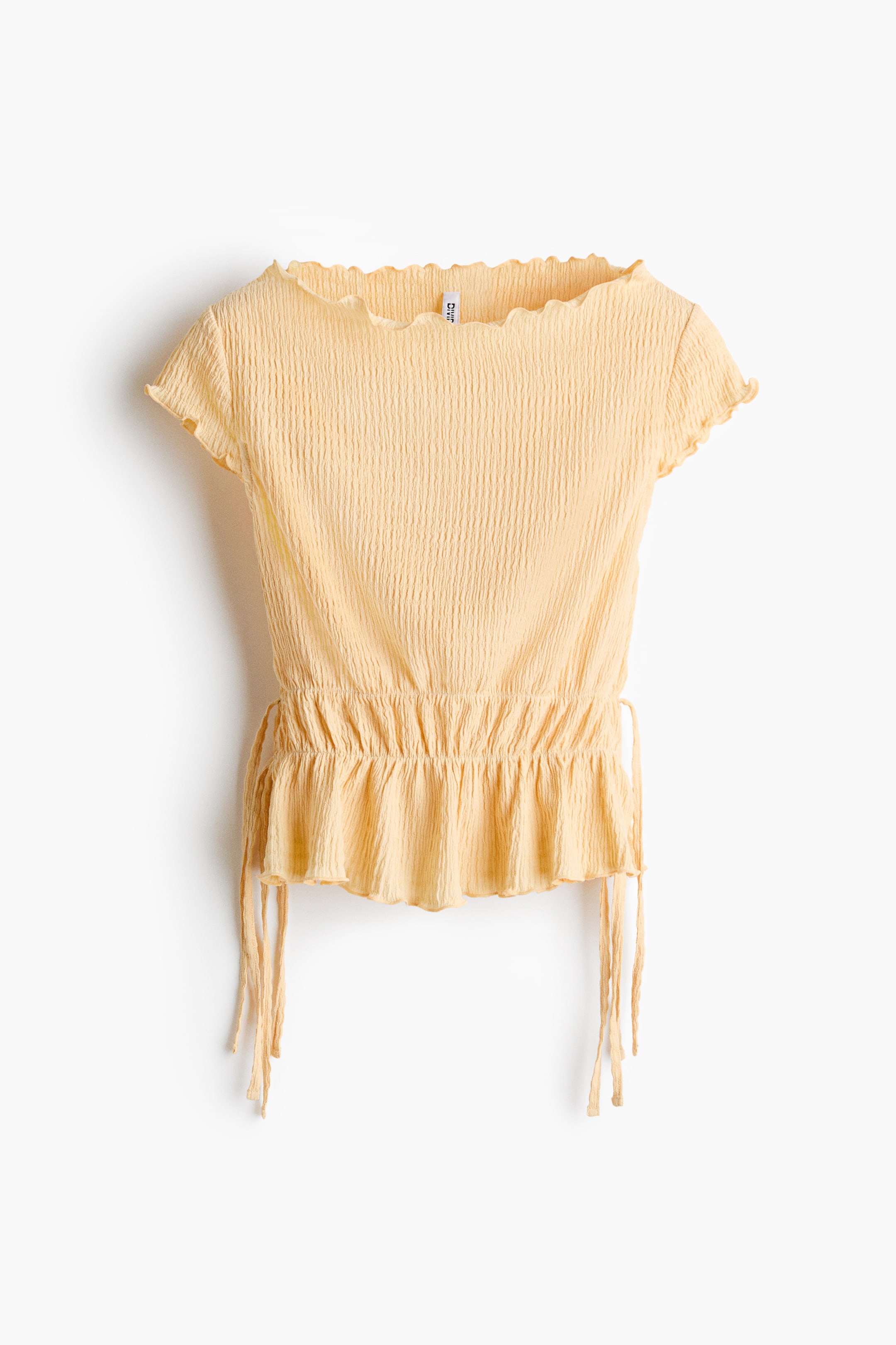 View larger image: A light yellow top shown from the FRONT, featuring a crinkled texture. It has a ruffled neckline and short sleeves, with an elasticized waist that creates a ruffled peplum hem and drawstrings at the sides.