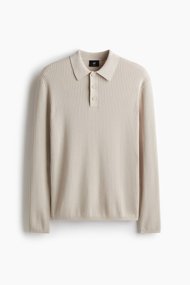 A light beige, long-sleeved polo shirt is being displayed from the front, featuring a vertical rib-knit texture, a pointed collar, a three-button placket, ribbed cuffs, and a ribbed hem. - 1