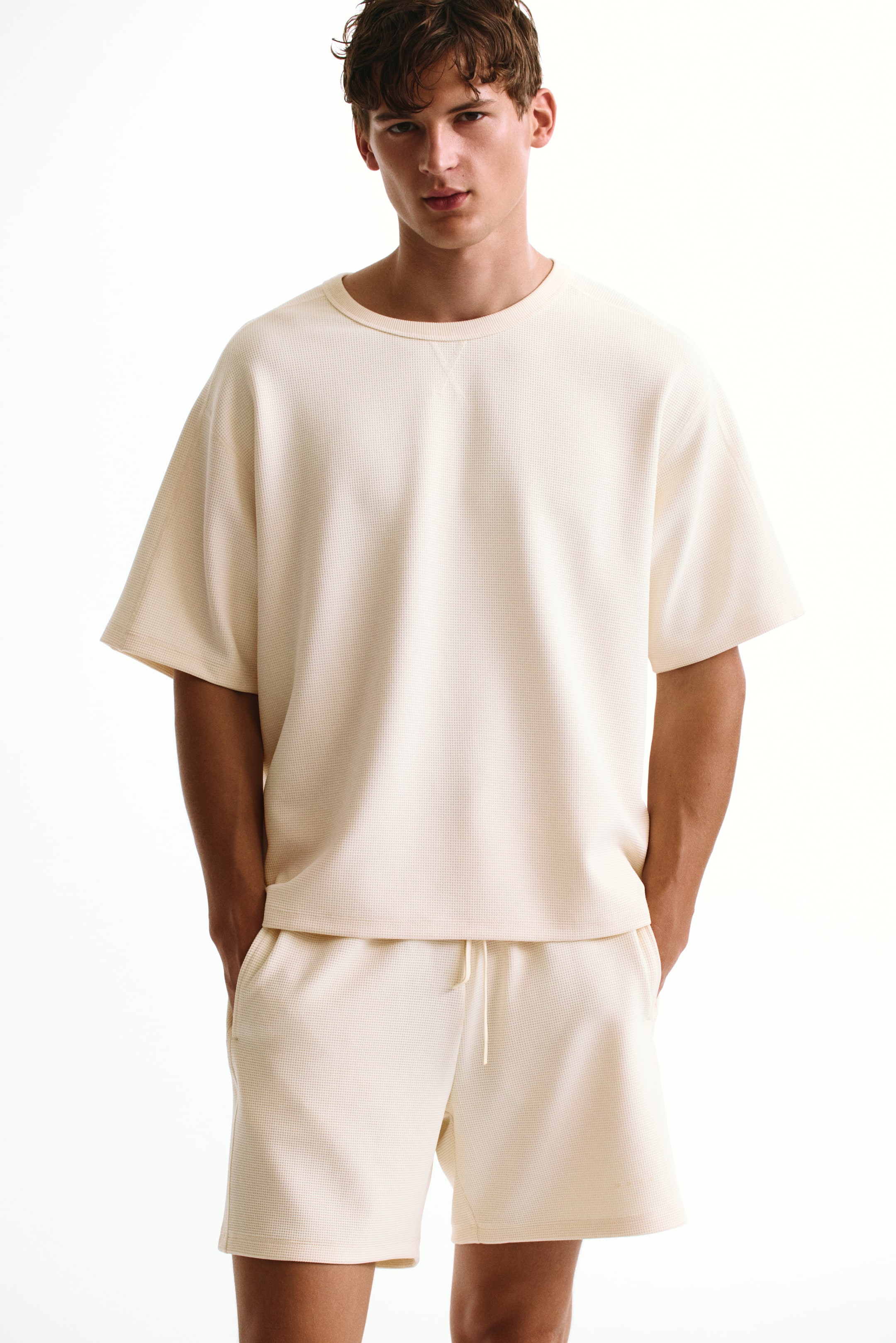 View larger image: The model is wearing a cream-colored, relaxed-fit waffle-knit sports T-shirt. The T-shirt features a crew neck and short, wide sleeves, and is styled with matching waffle-knit shorts.