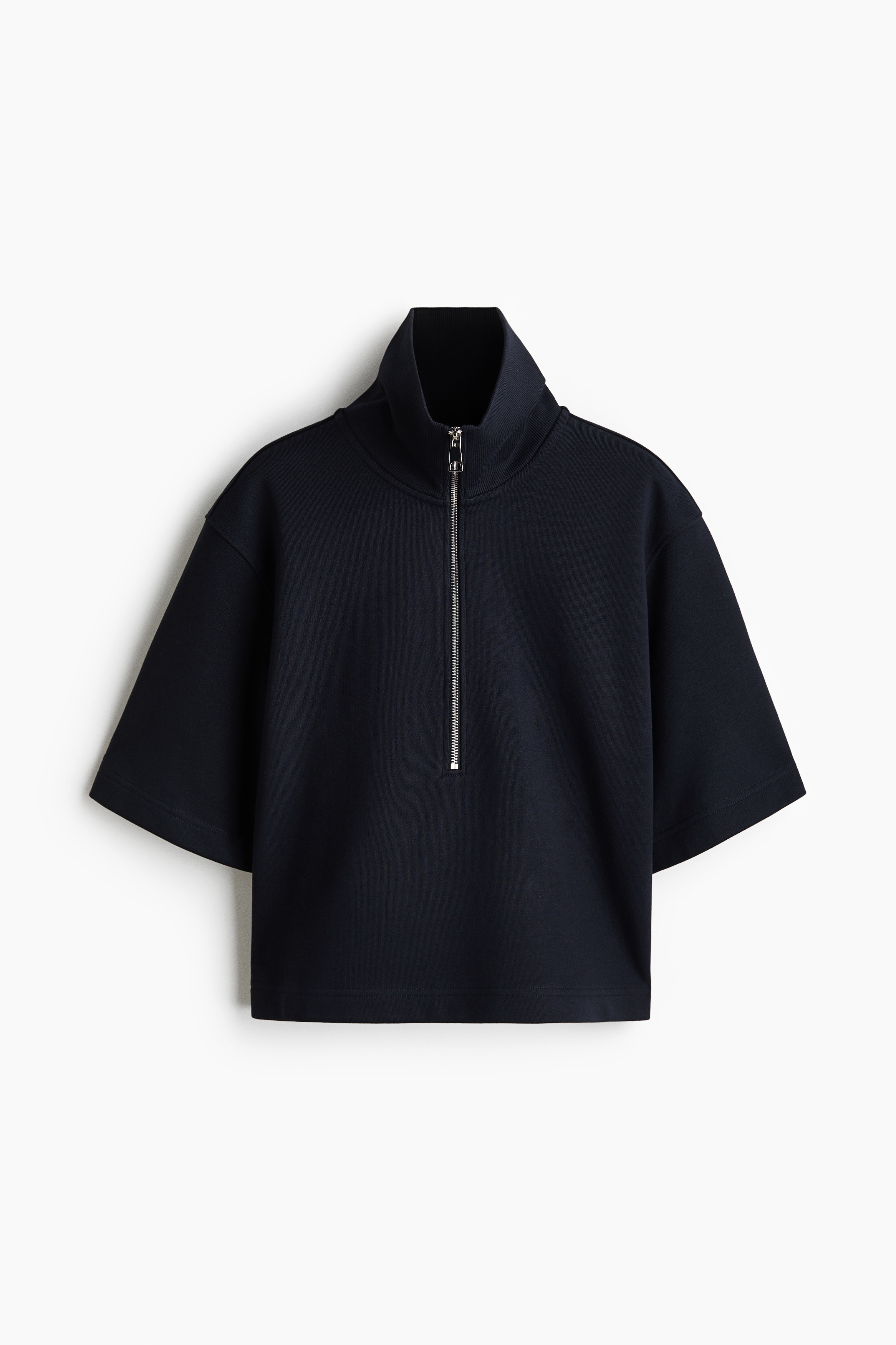 A dark blue polo shirt in lightweight sweat fabric, featuring a rib-trimmed collar, a half-zip front, dropped shoulders, and elbow-length sleeves, is worn by the model. The cropped-style shirt is layered over a white top and styled with beige trousers.